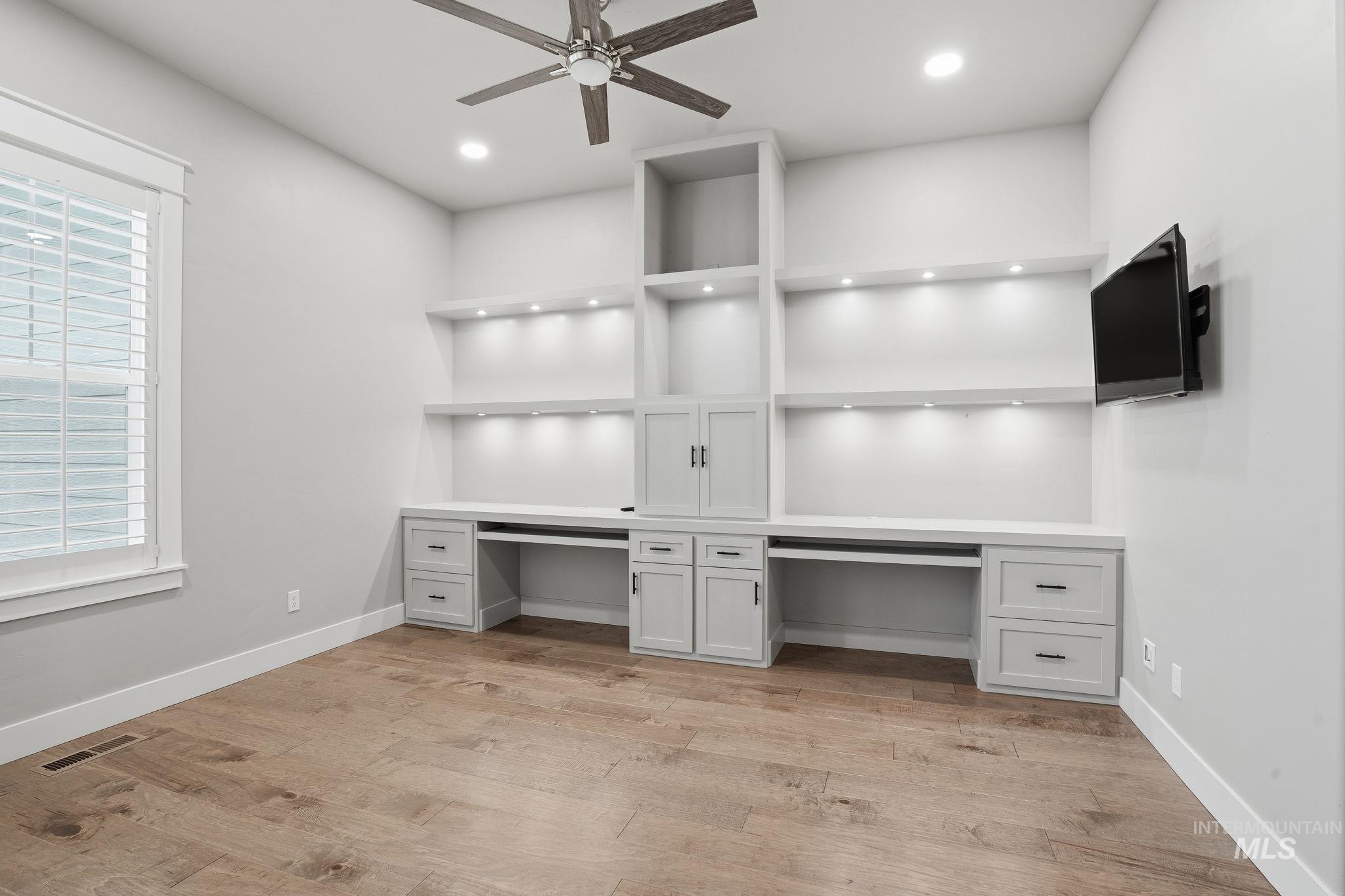 Unfurnished office featuring light wood finished floors, built in desk, ceiling fan, and recessed lighting