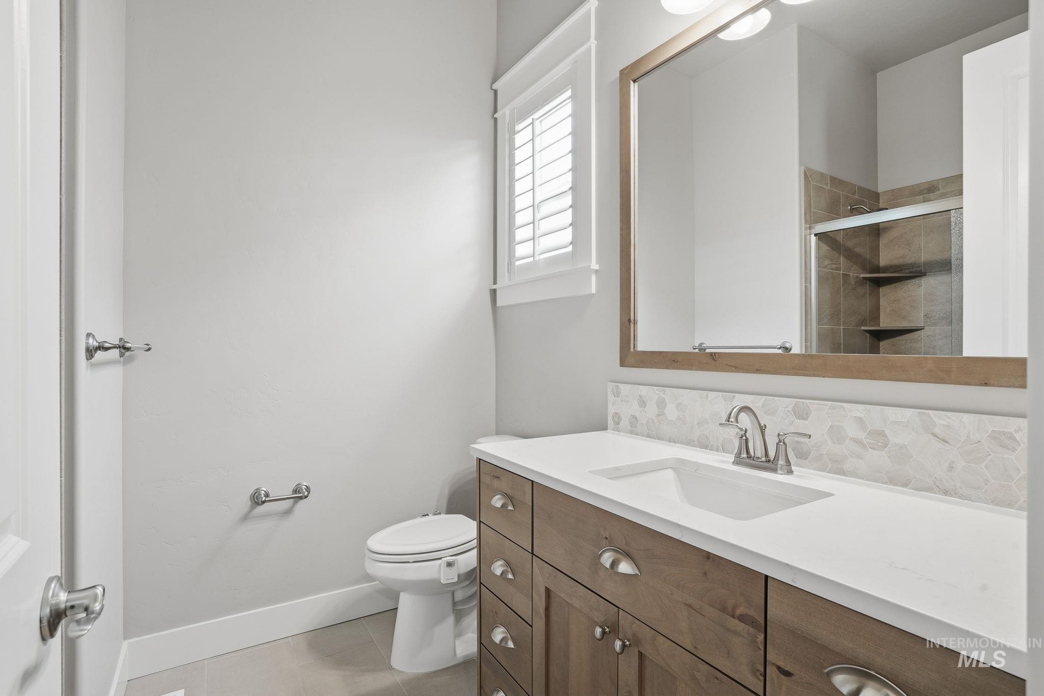 Bathroom featuring vanity, a shower stall, light tile patterned flooring, and backsplash