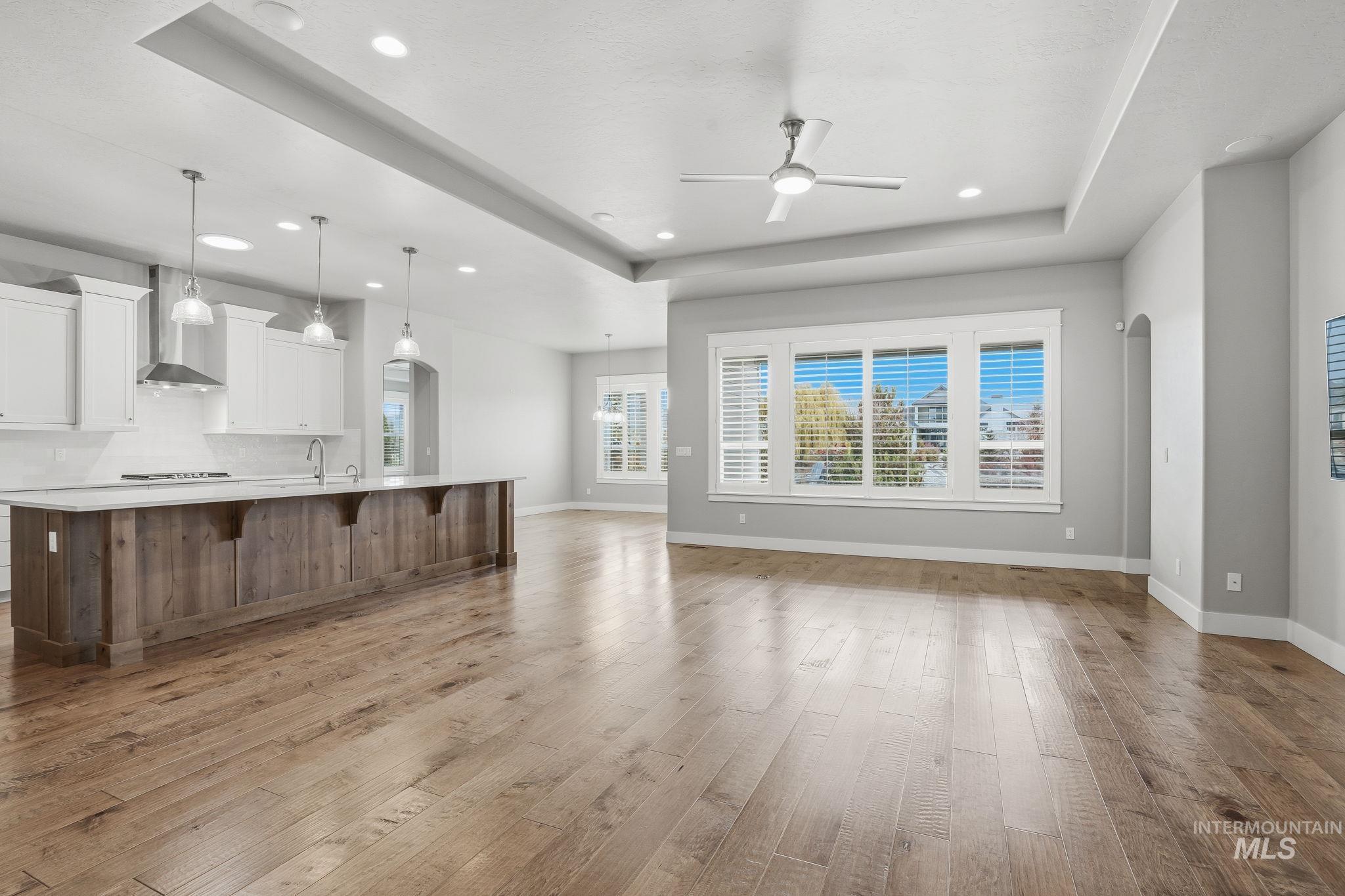 Unfurnished living room featuring a tray ceiling, light wood finished floors, a ceiling fan, recessed lighting, and arched walkways