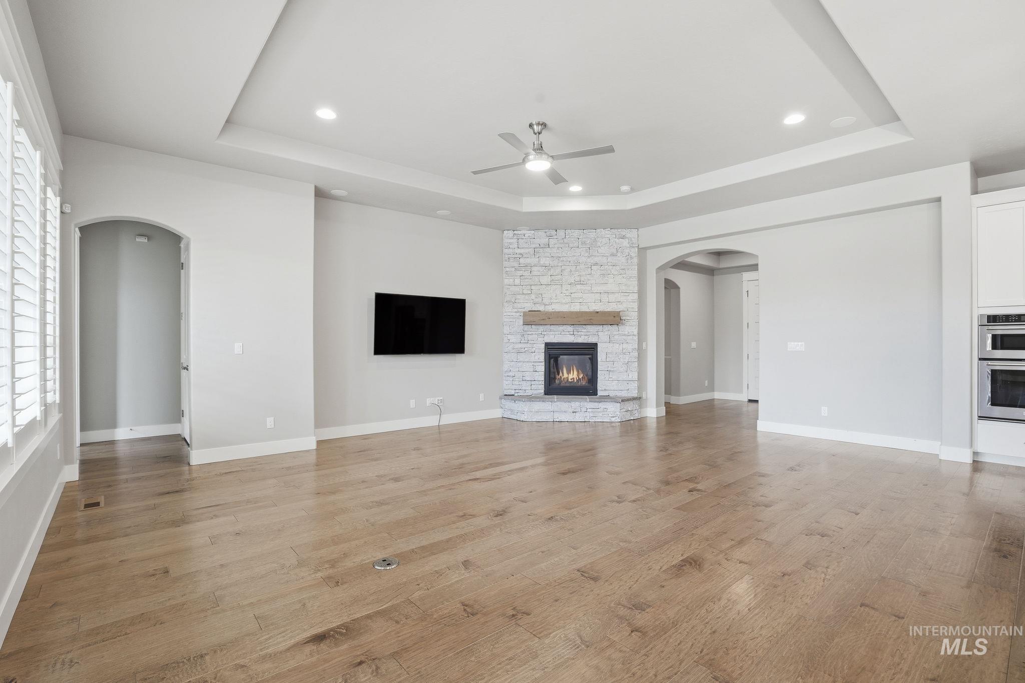 Unfurnished living room with arched walkways, light wood-type flooring, a raised ceiling, and recessed lighting