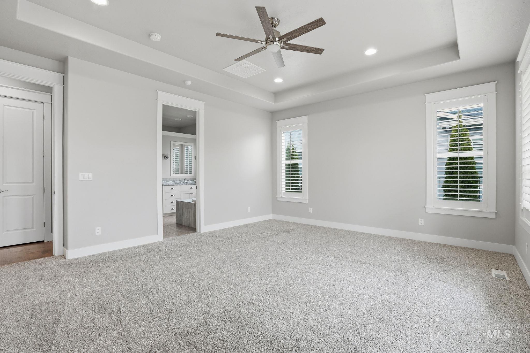 Unfurnished bedroom featuring a tray ceiling, light colored carpet, ensuite bath, recessed lighting, and ceiling fan