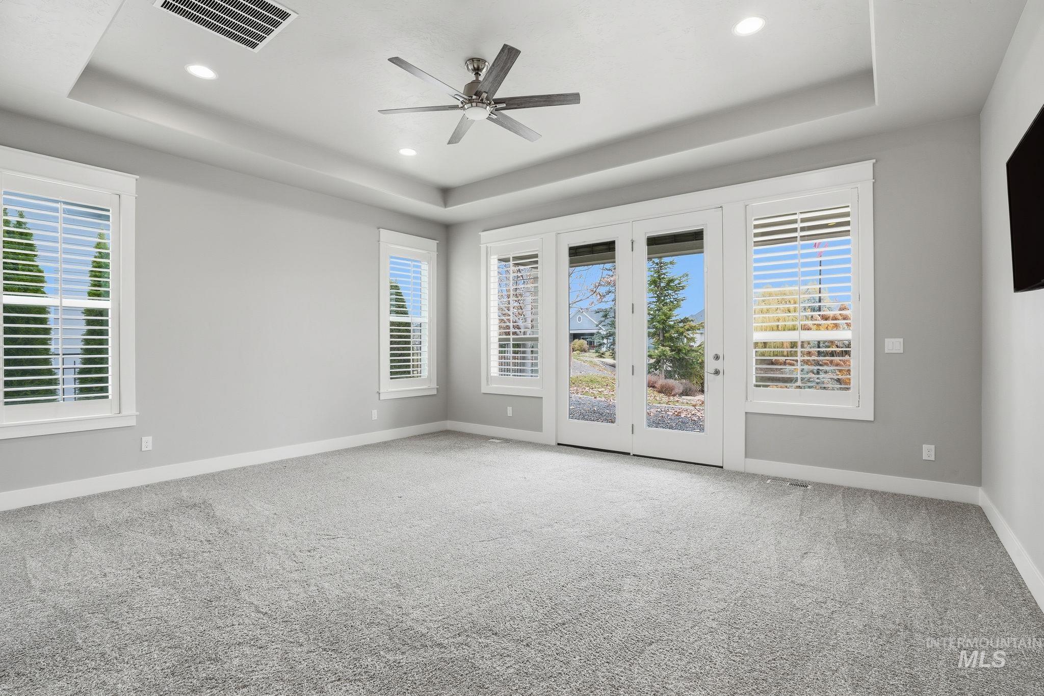 Empty room featuring a raised ceiling, plenty of natural light, light colored carpet, a ceiling fan, and recessed lighting