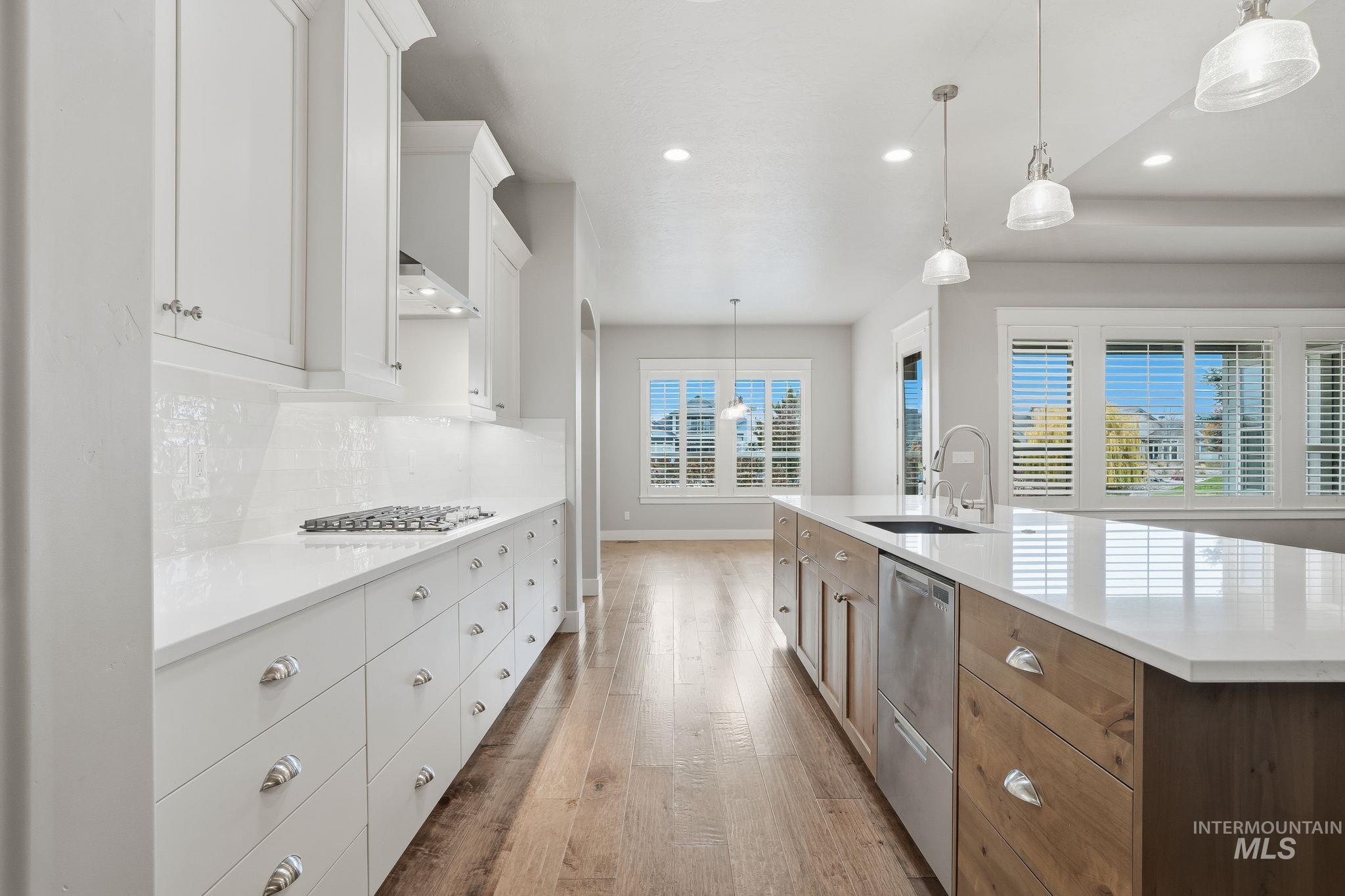 Kitchen featuring white cabinets, hanging light fixtures, wood finished floors, appliances with stainless steel finishes, and decorative backsplash