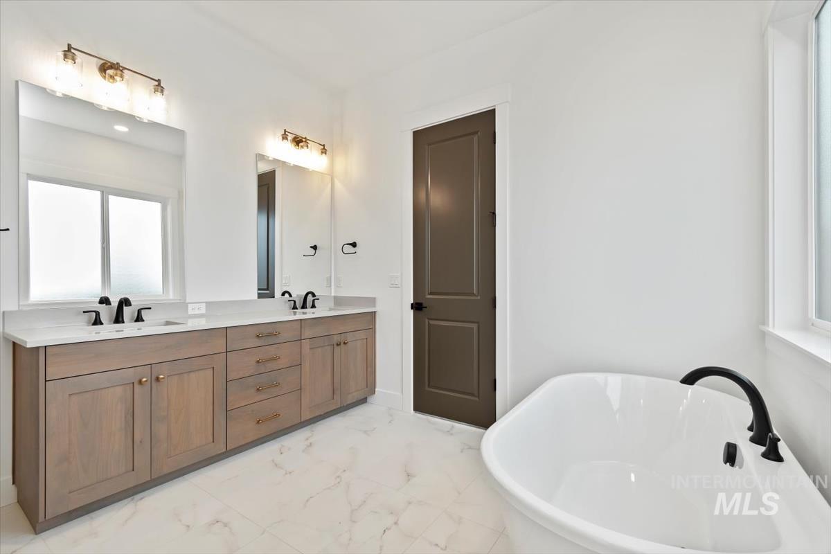 Bathroom featuring light marble finish floors, a freestanding tub, and double vanity