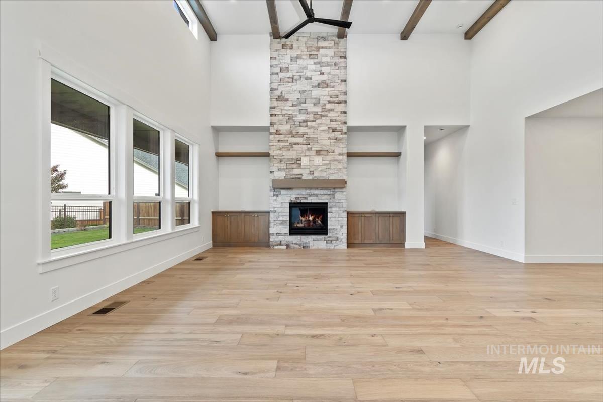 Unfurnished living room with light wood-style flooring, a stone fireplace, beam ceiling, and a high ceiling