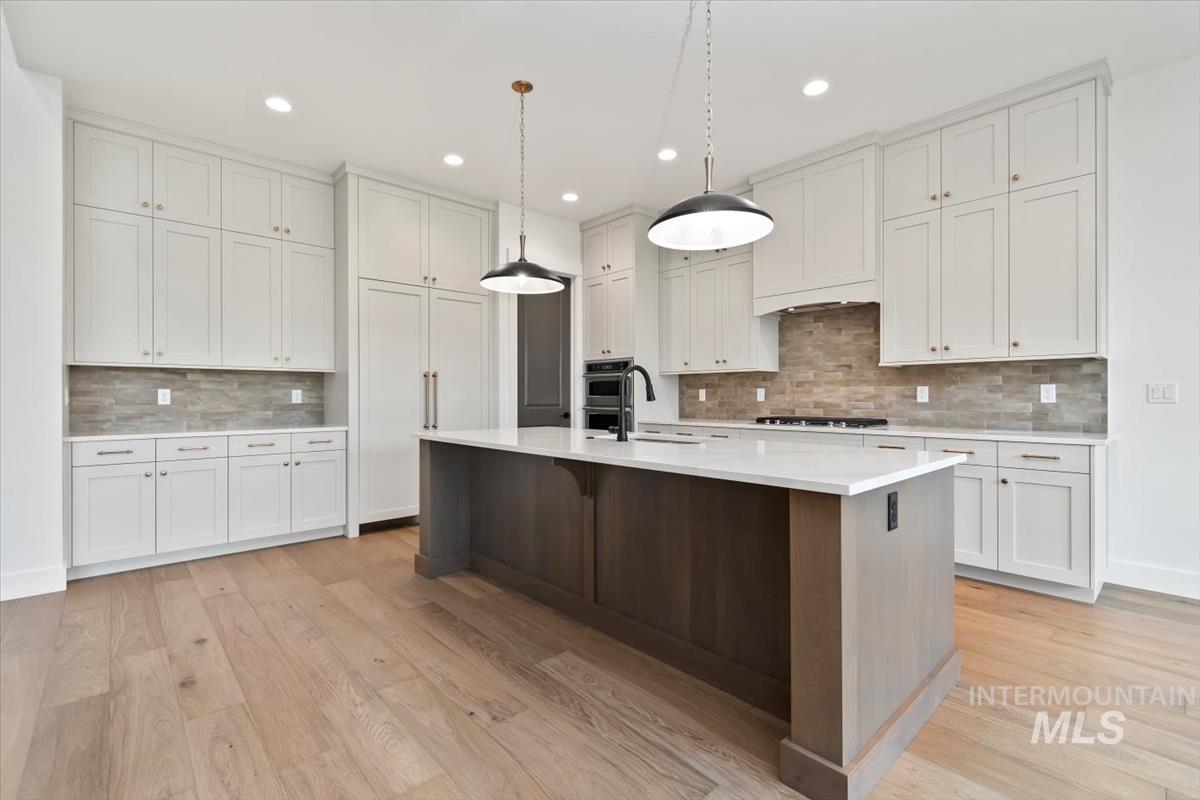 Kitchen featuring white cabinets, an island with sink, tasteful backsplash, hanging light fixtures, and recessed lighting