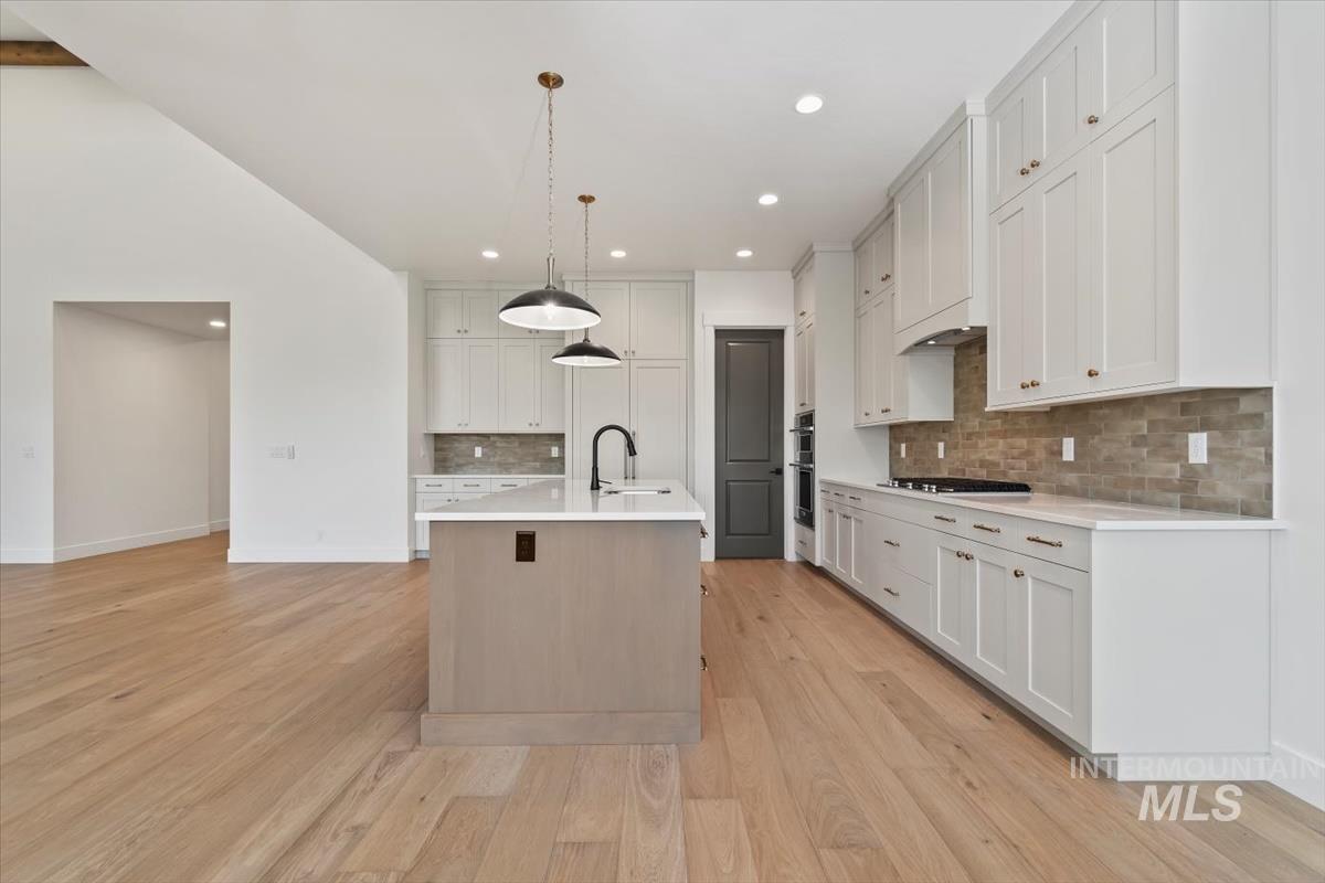 Kitchen with hanging light fixtures, an island with sink, light wood-type flooring, light stone countertops, and recessed lighting