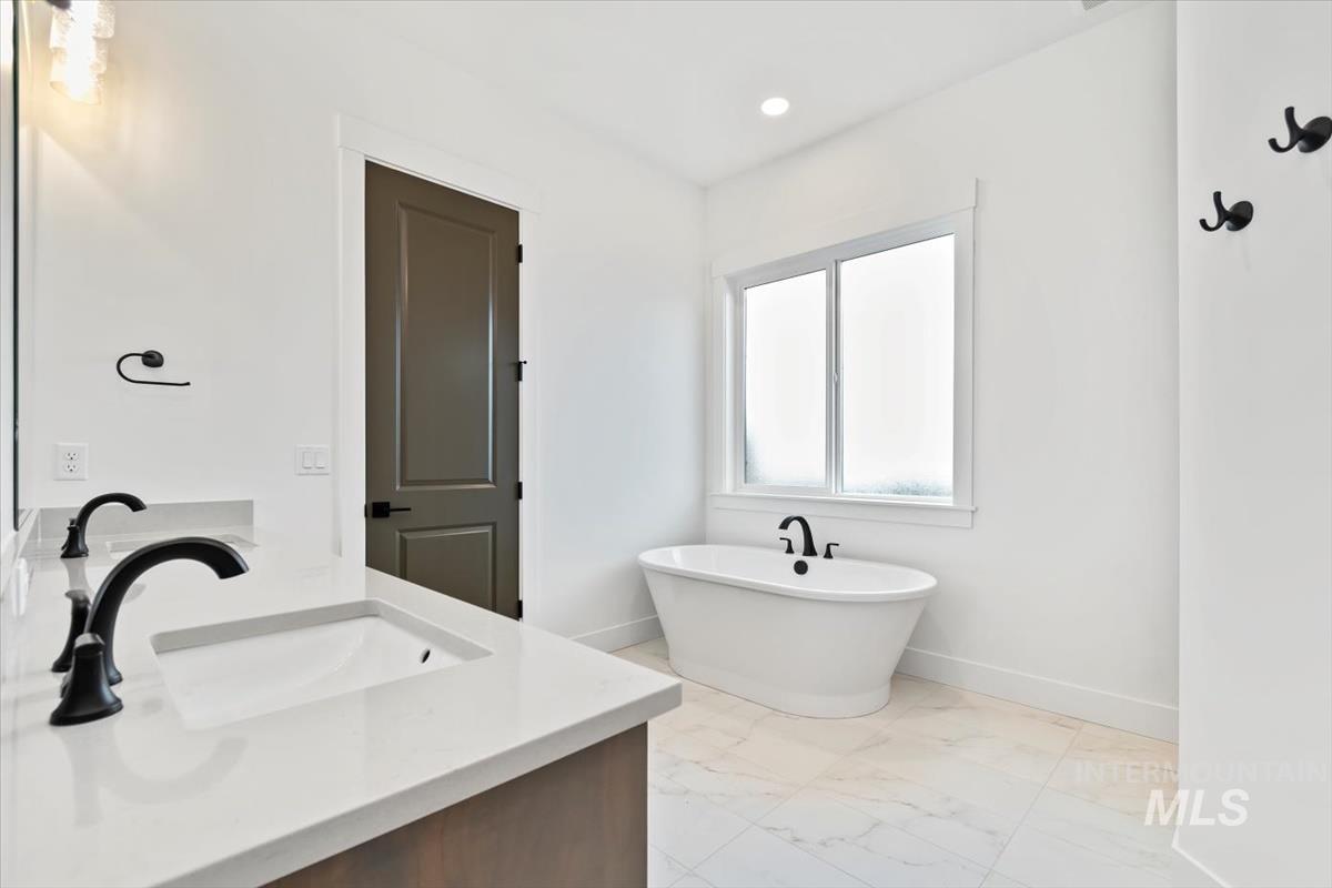 Full bath featuring double vanity, a soaking tub, light marble finish flooring, and recessed lighting