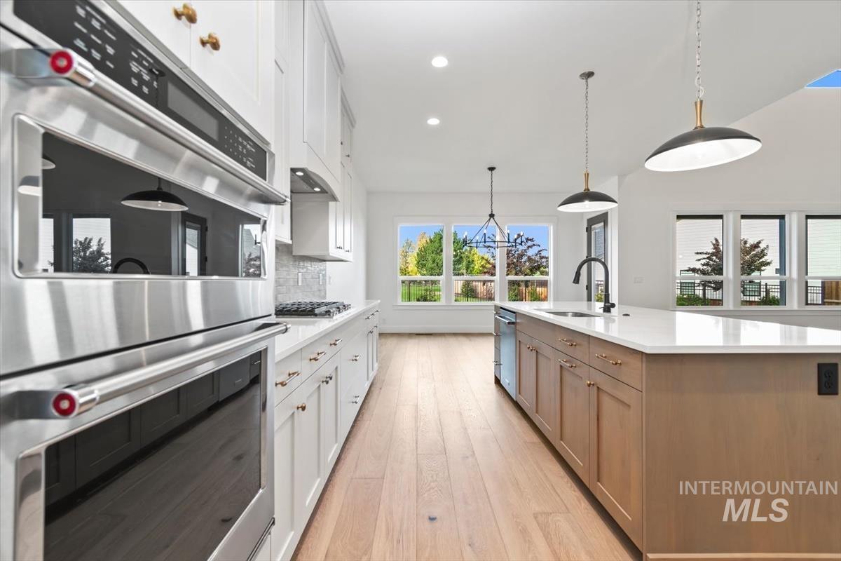 Kitchen featuring appliances with stainless steel finishes, white cabinetry, decorative light fixtures, backsplash, and light wood-style floors