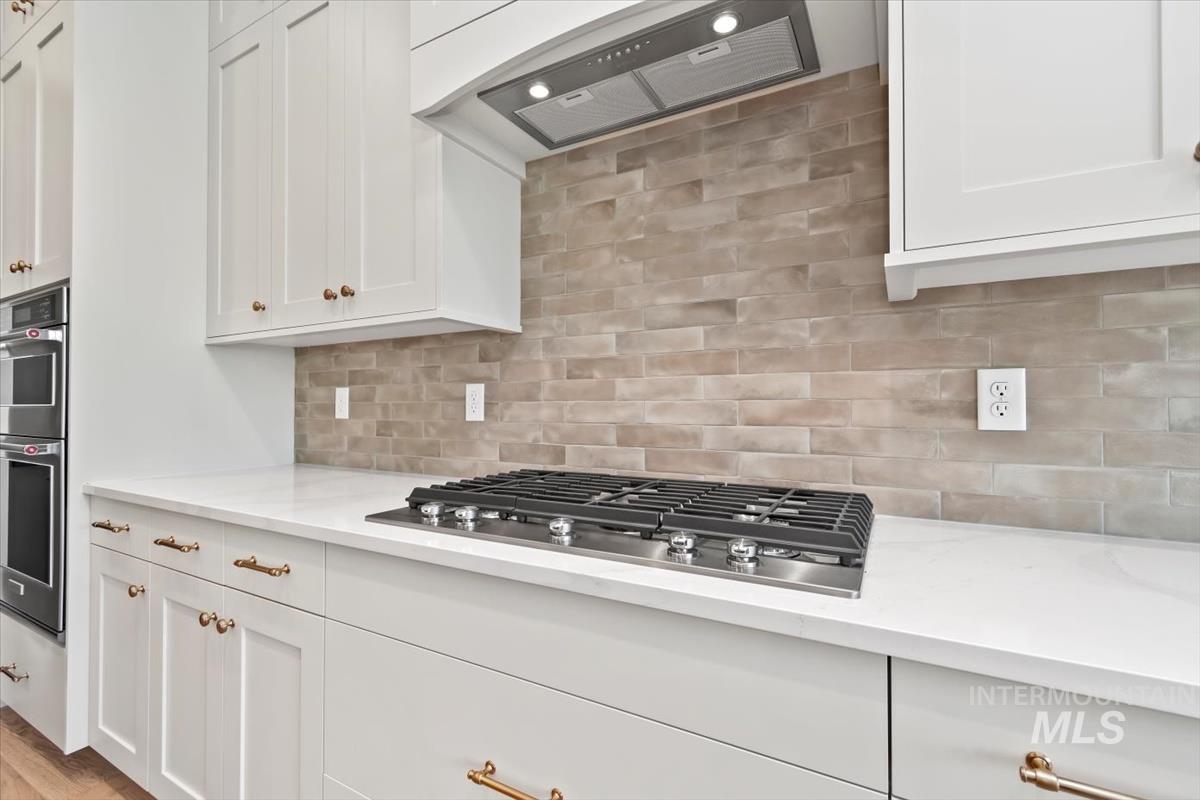 Kitchen with white cabinets, wall chimney range hood, backsplash, and appliances with stainless steel finishes