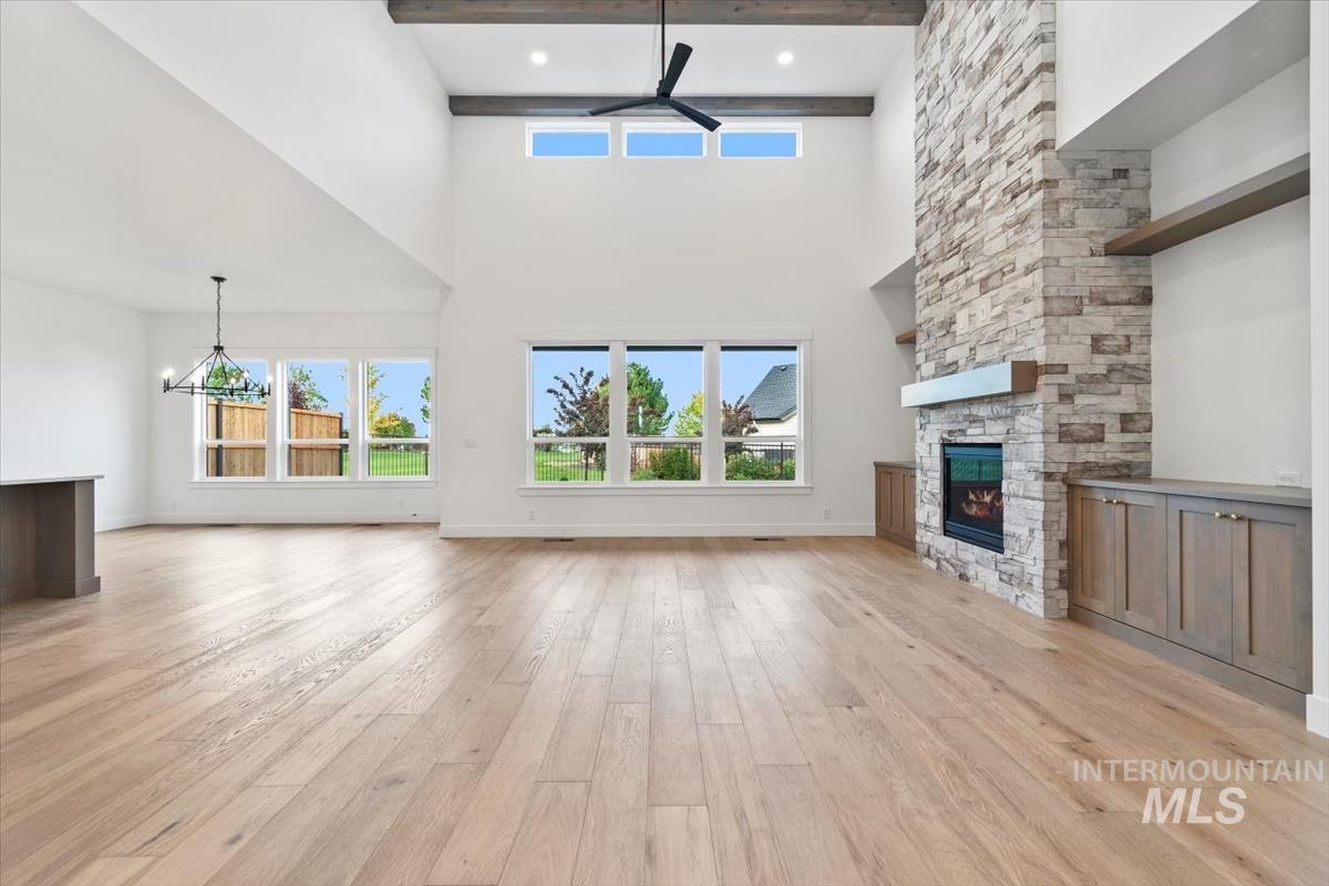 Unfurnished living room with a fireplace, light wood-style flooring, beamed ceiling, and a chandelier