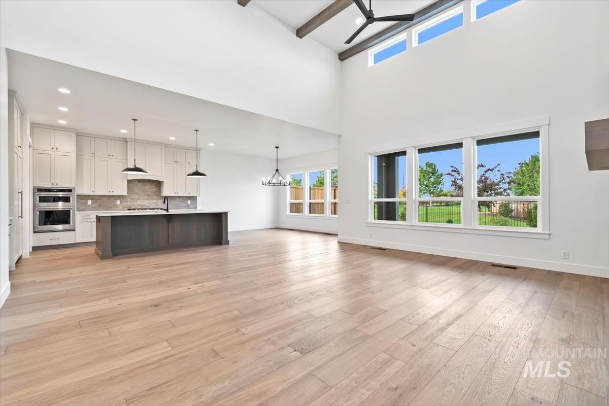 Unfurnished living room with a chandelier, healthy amount of natural light, light wood-type flooring, and a towering ceiling