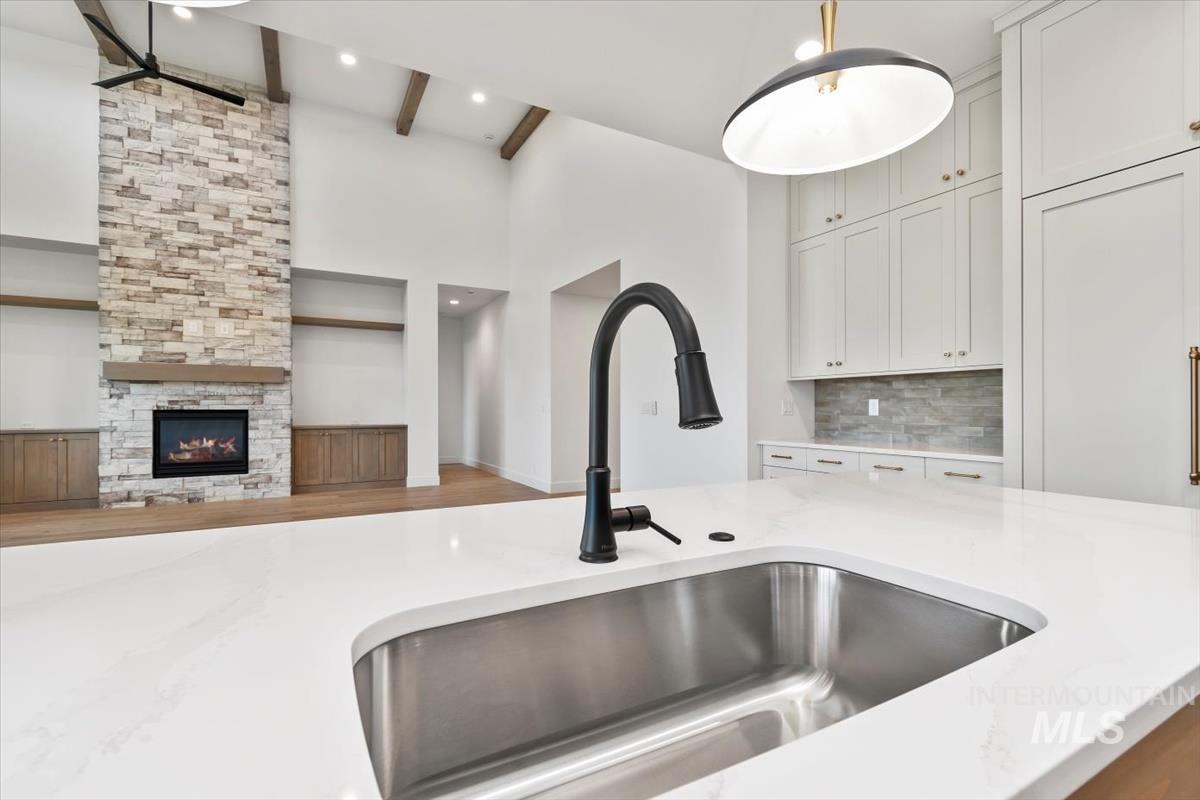 Kitchen with light stone counters, backsplash, wood finished floors, open floor plan, and beamed ceiling