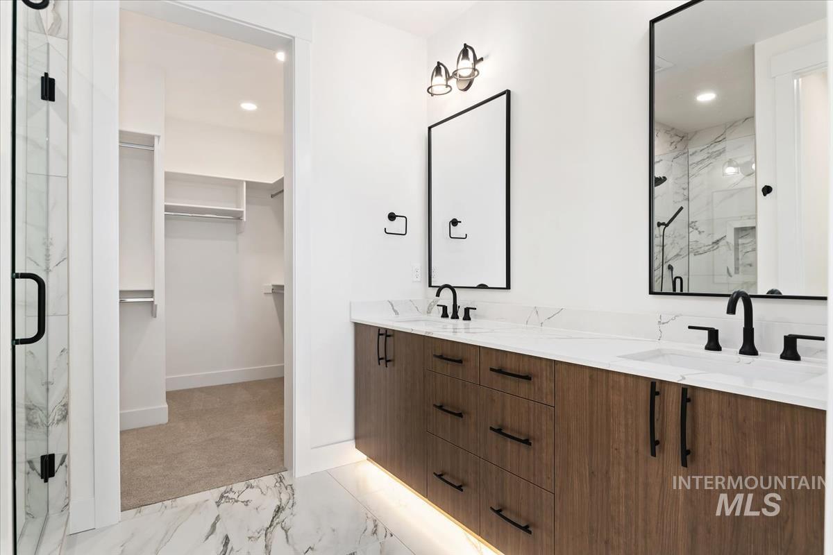 Bathroom with a walk in closet, a marble finish shower, light marble finish flooring, double vanity, and recessed lighting