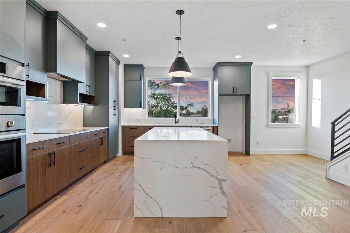 Kitchen featuring a center island, light stone counters, pendant lighting, light wood-style flooring, and recessed lighting