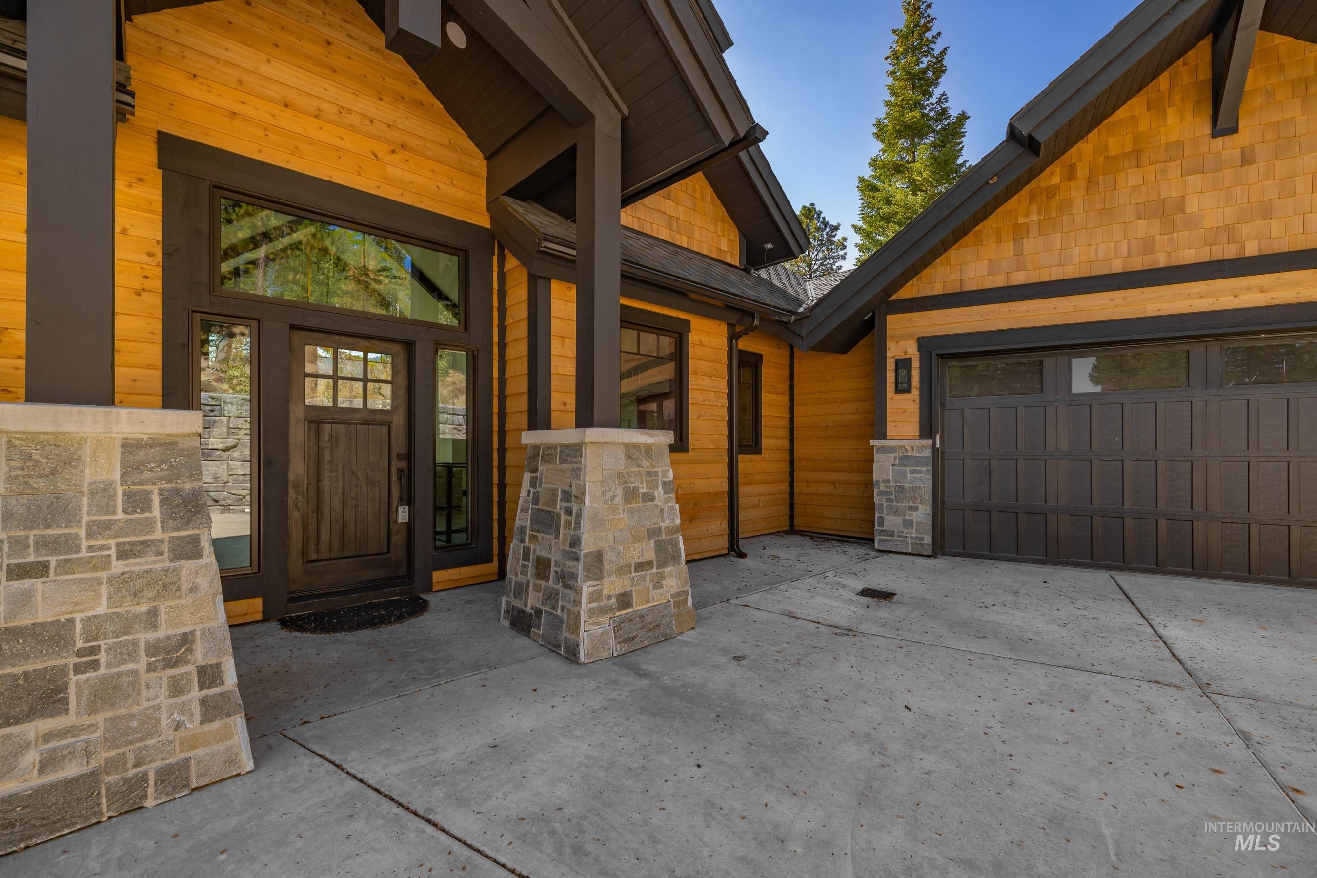 Entrance to property featuring stone siding, a garage, and driveway