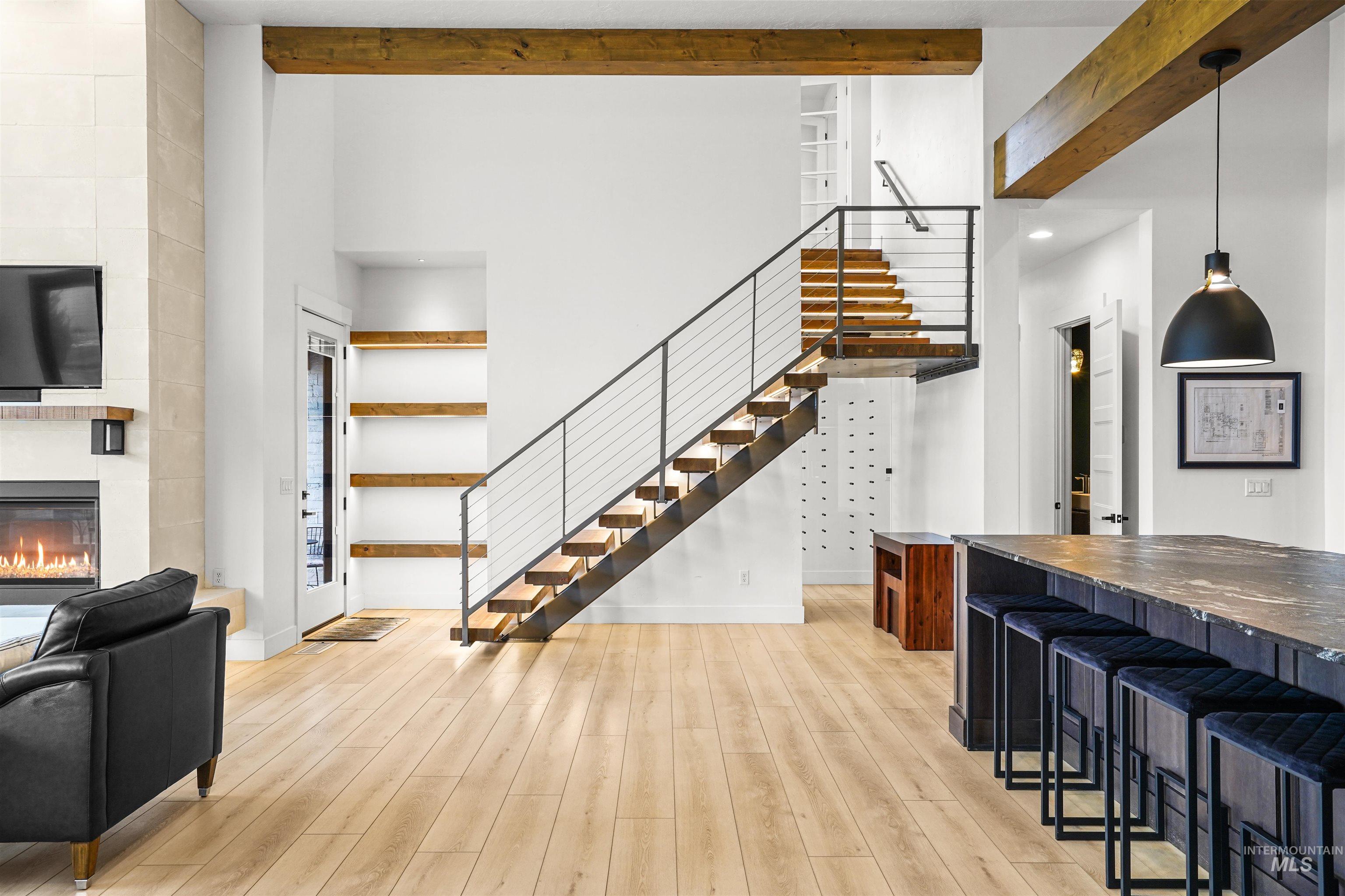 Living room with stairway, a fireplace, a towering ceiling, light wood-style floors, and beam ceiling