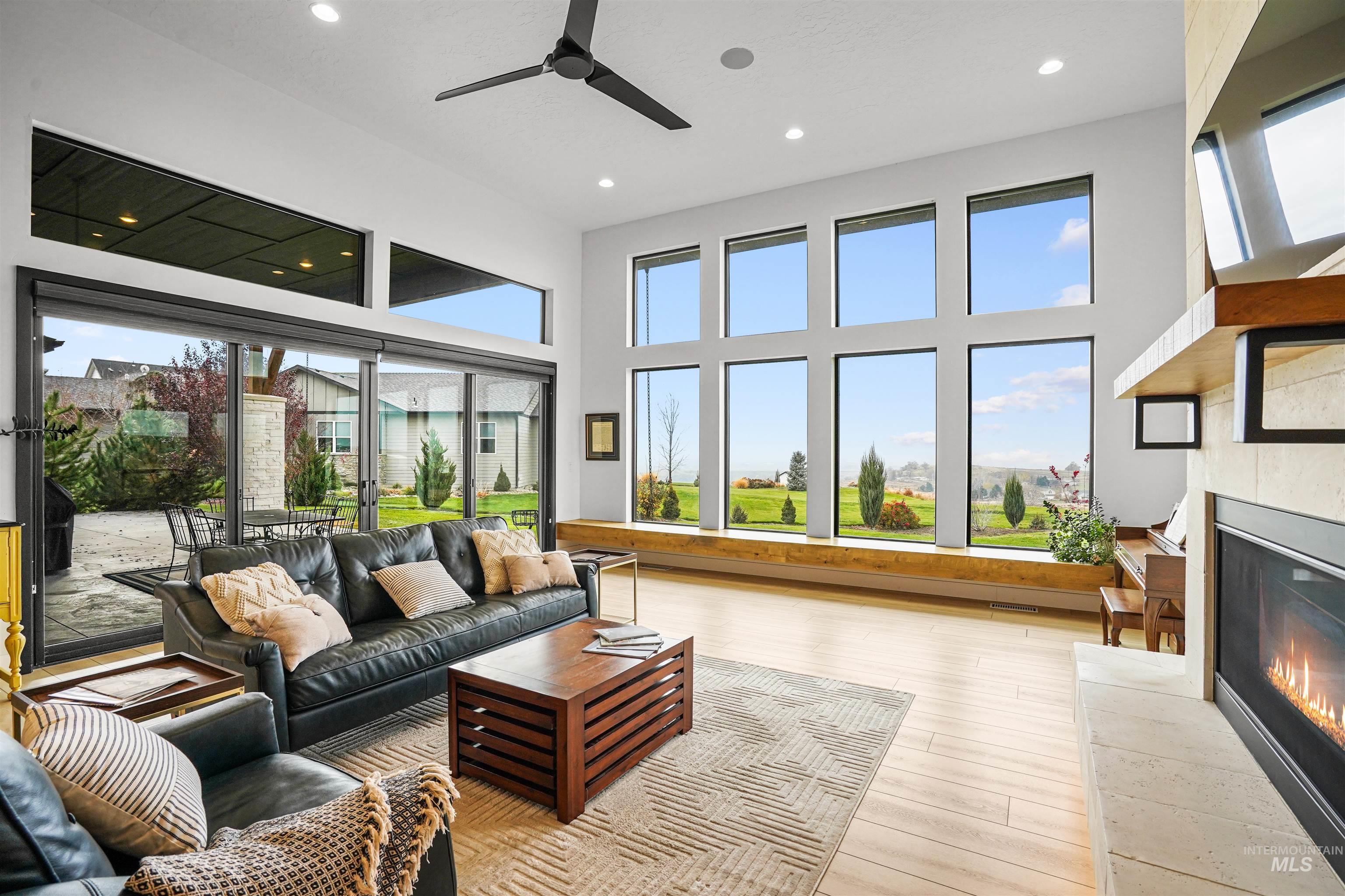 Living room with a glass covered fireplace, light wood-style flooring, a ceiling fan, a towering ceiling, and recessed lighting