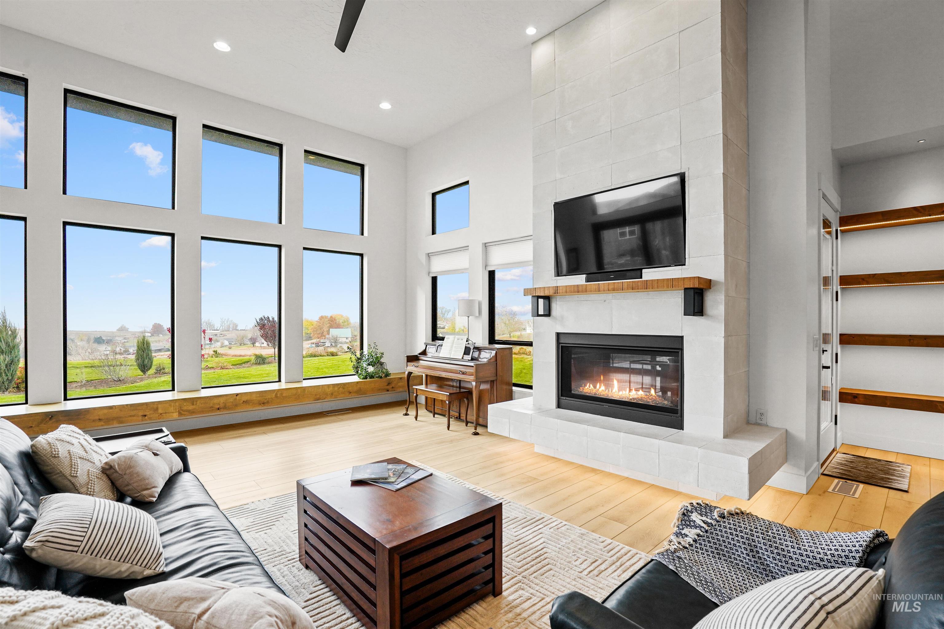 Living room featuring wood-type flooring, a towering ceiling, a tile fireplace, ceiling fan, and recessed lighting