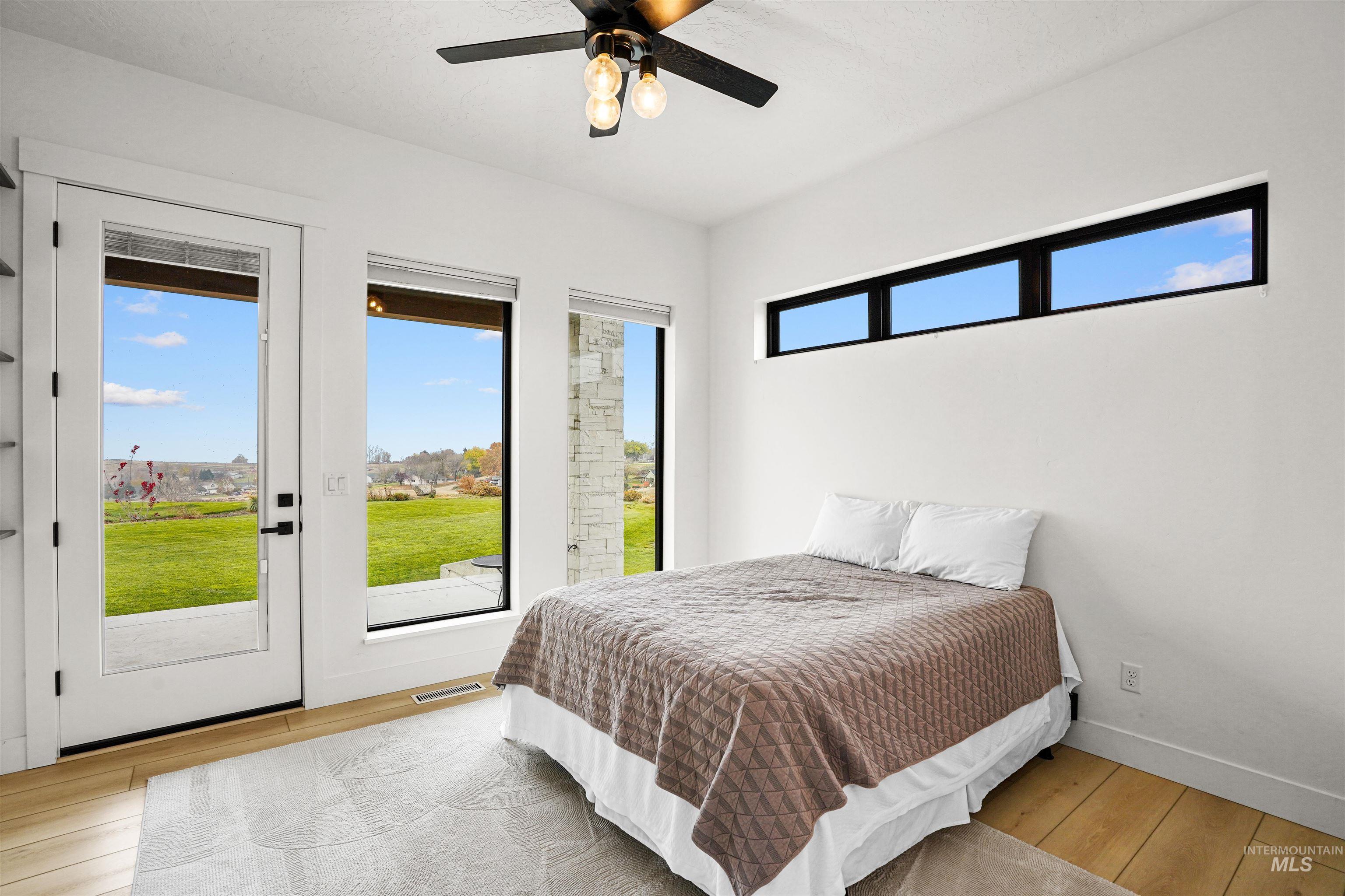 Bedroom with multiple windows, access to exterior, light wood finished floors, and ceiling fan