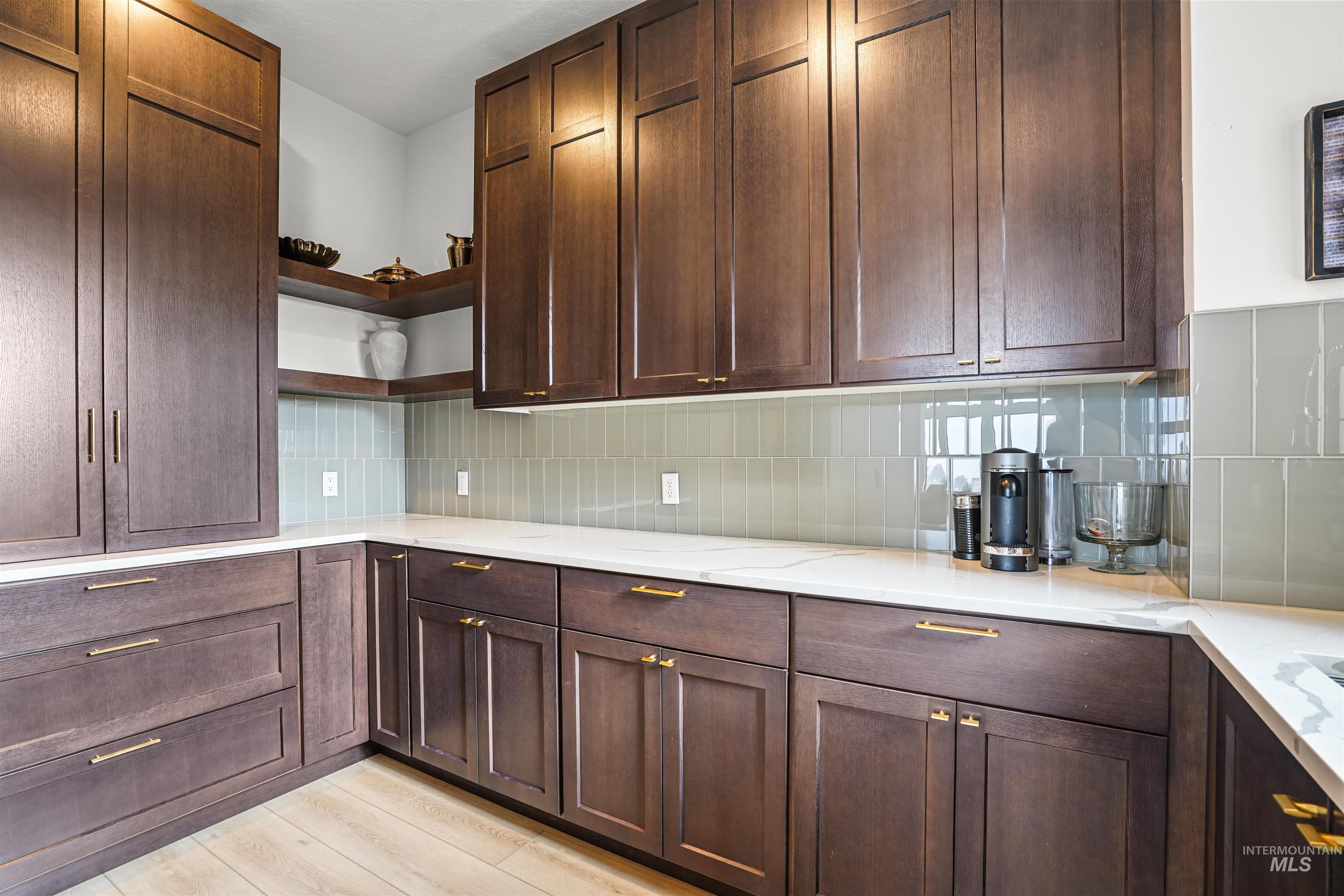 Kitchen with open shelves, dark brown cabinetry, light stone countertops, tasteful backsplash, and light wood-style flooring
