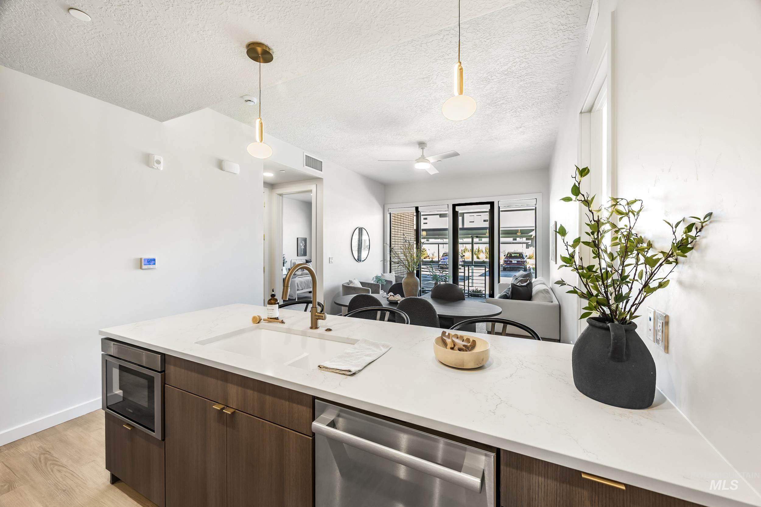 Kitchen featuring decorative light fixtures, open floor plan, stainless steel appliances, dark brown cabinetry, and a textured ceiling