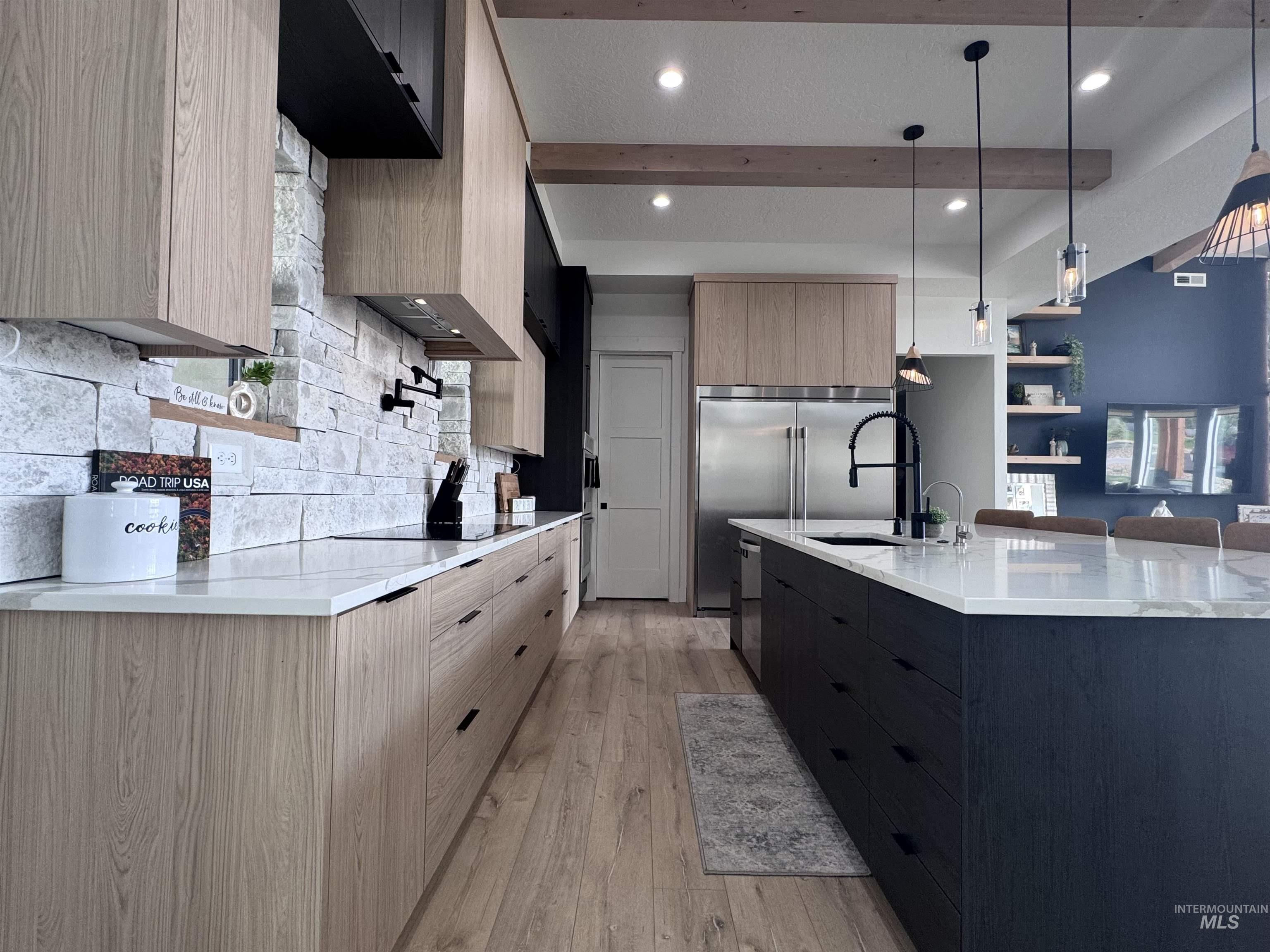 Kitchen with modern cabinets, light brown cabinetry, light stone countertops, decorative light fixtures, and beamed ceiling