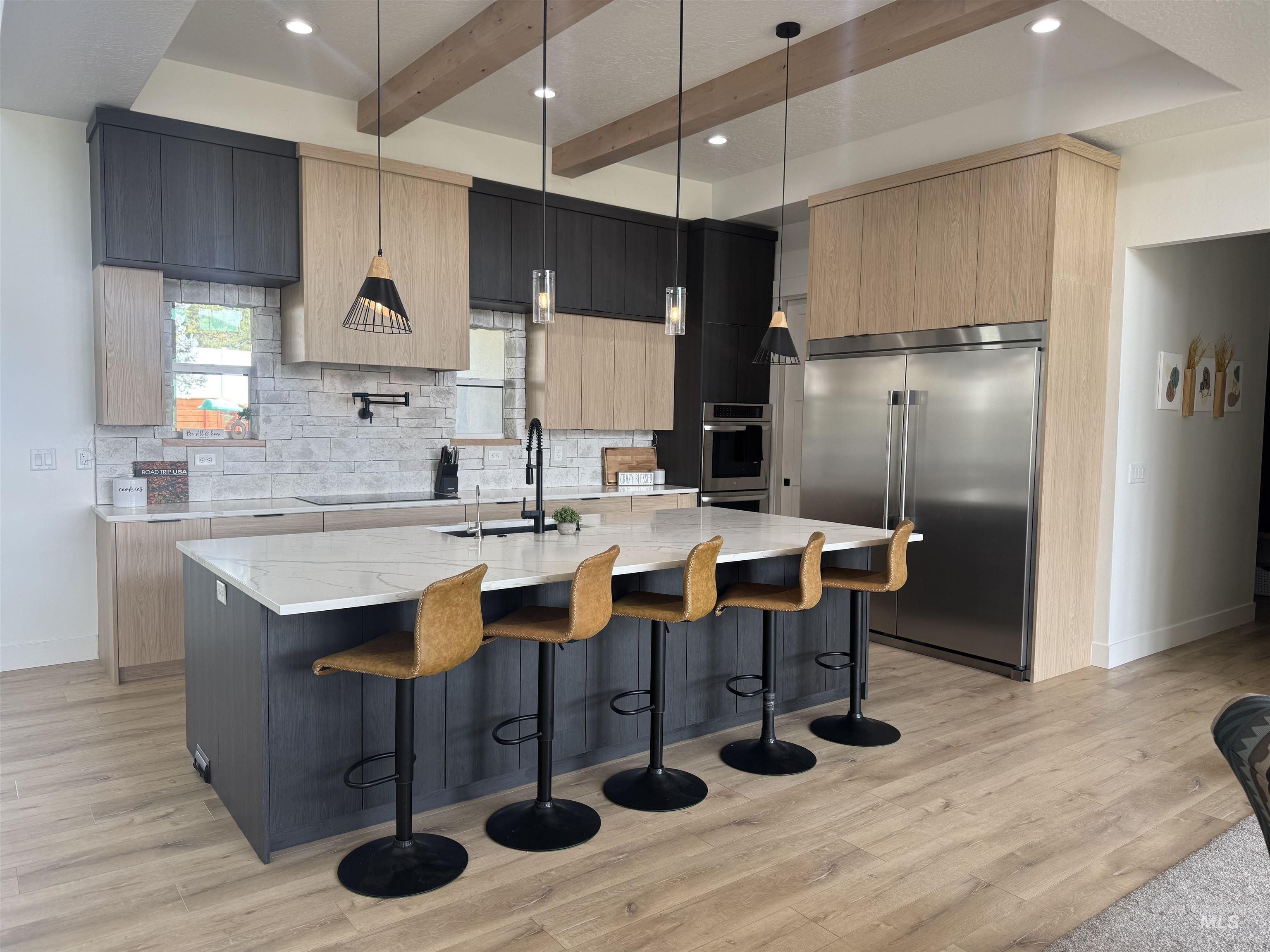 Kitchen with light brown cabinets, hanging light fixtures, a breakfast bar area, stainless steel appliances, and beamed ceiling