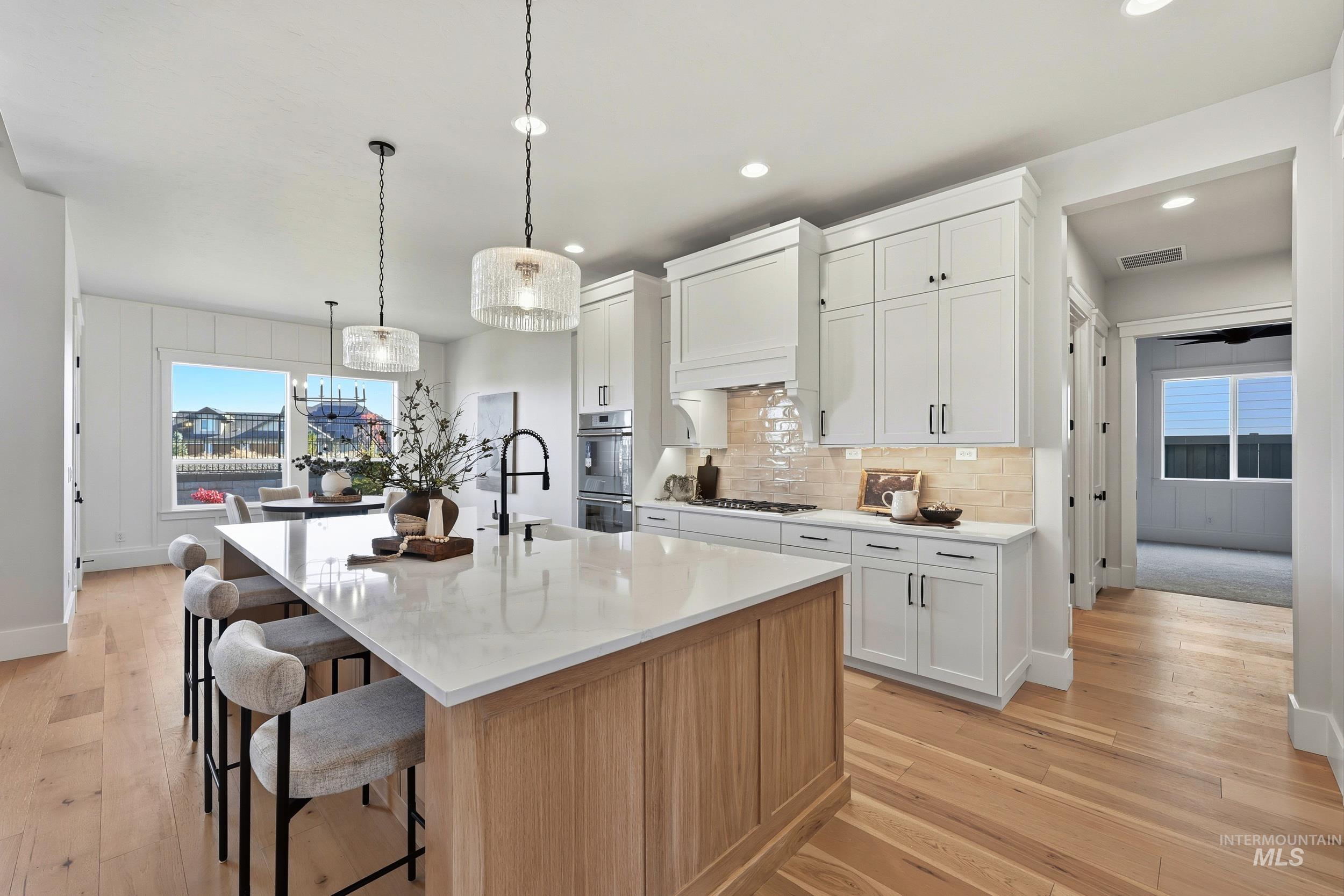 Kitchen with white cabinets, light wood-type flooring, a center island with sink, backsplash, and recessed lighting