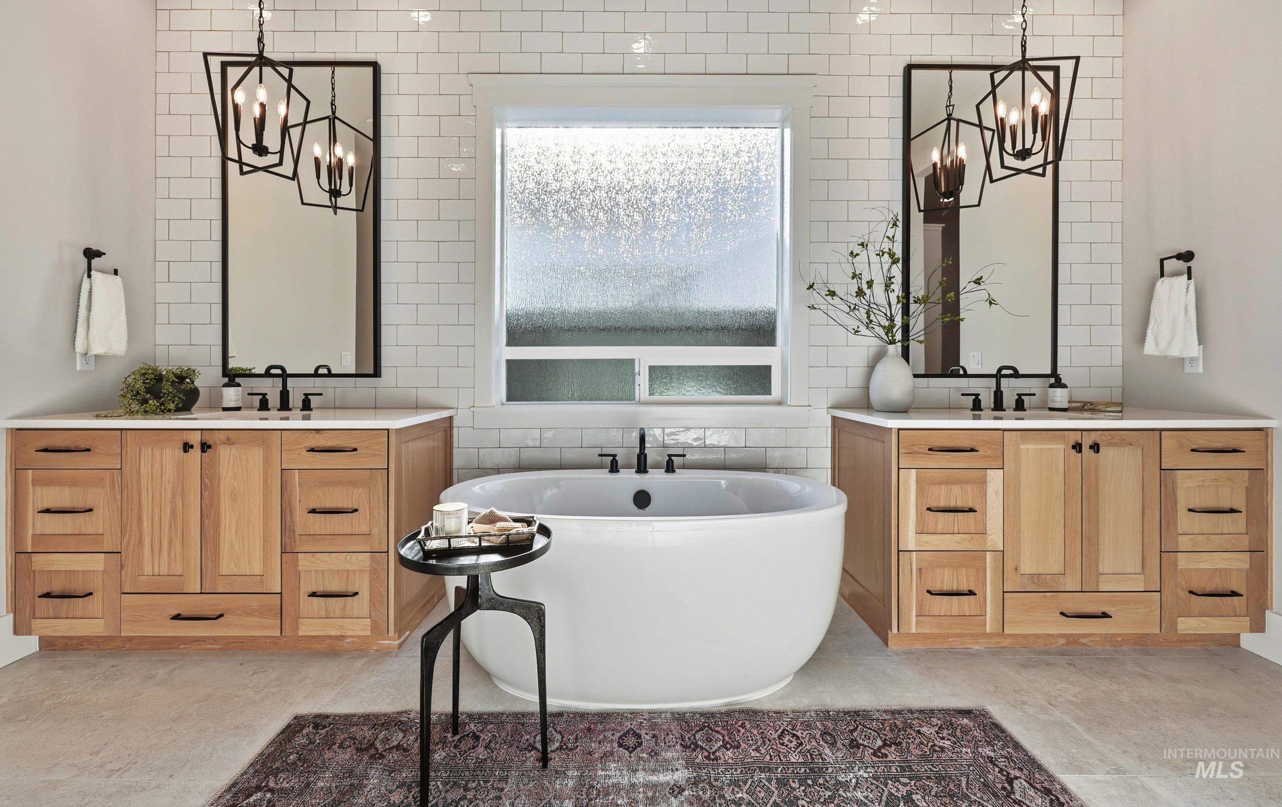 Bathroom with a chandelier, tile walls, a freestanding tub, two vanities, and tasteful backsplash