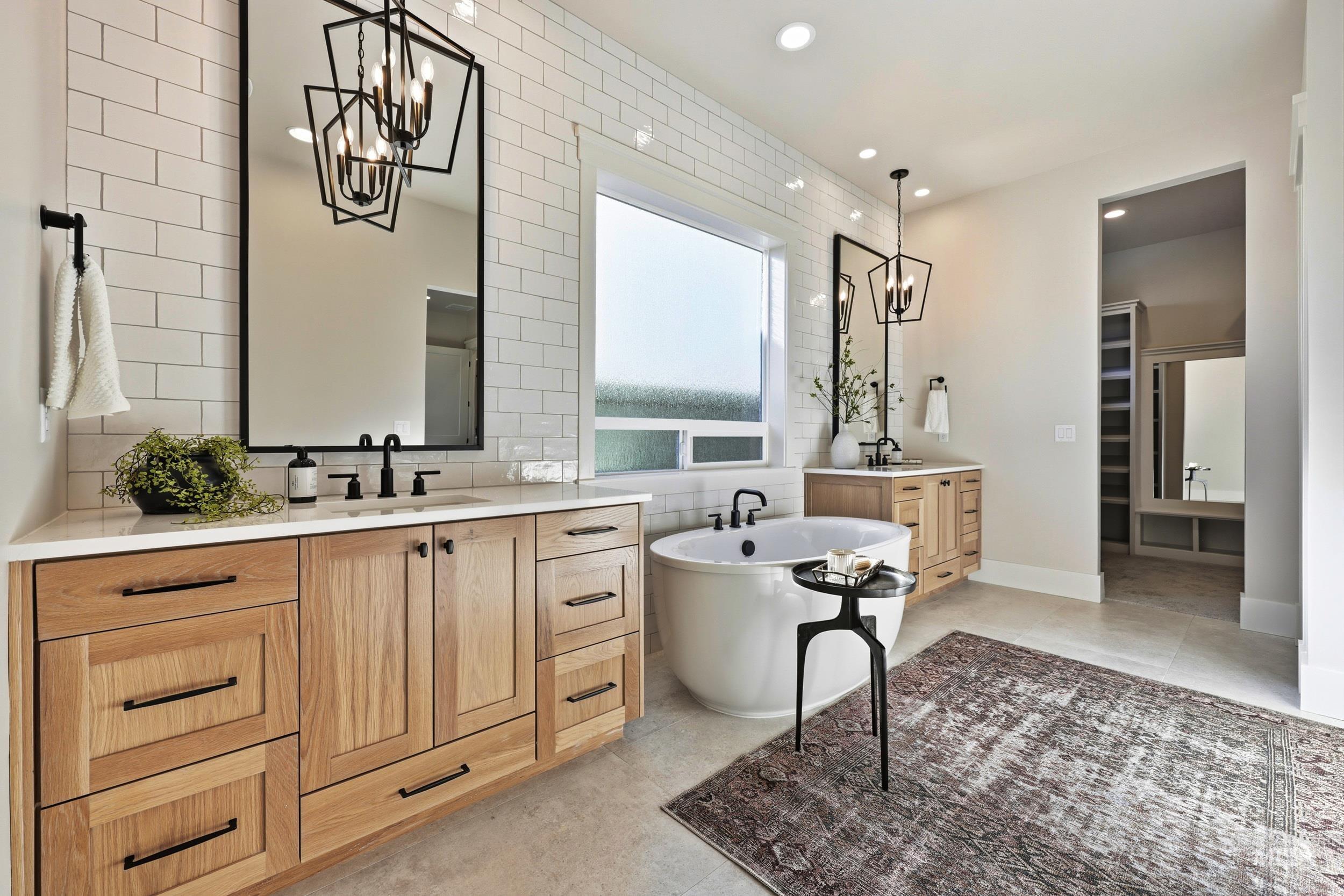 Bathroom featuring a chandelier, two vanities, a soaking tub, a spacious closet, and tasteful backsplash