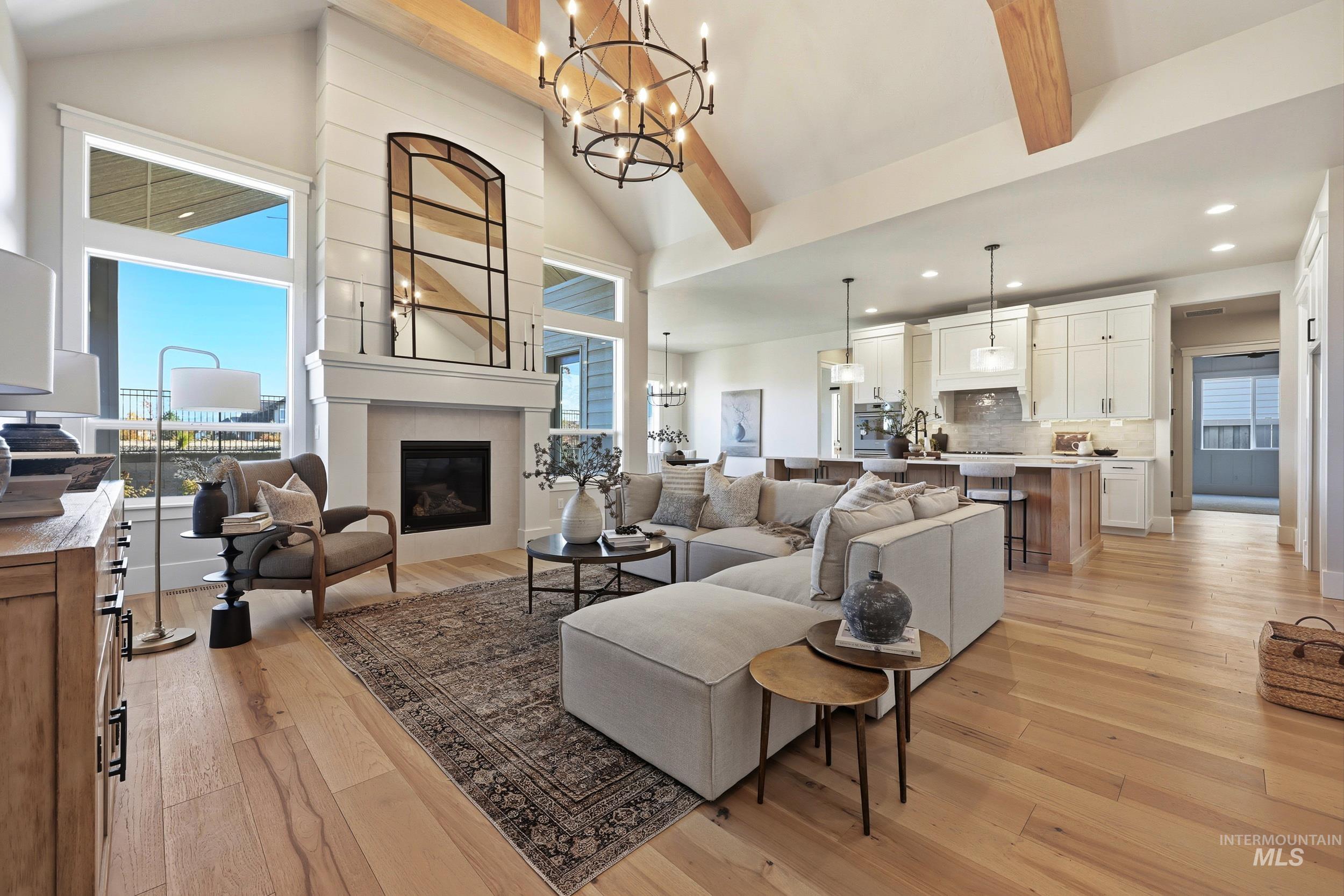Living room featuring a chandelier, light wood-style floors, a fireplace, beam ceiling, and high vaulted ceiling