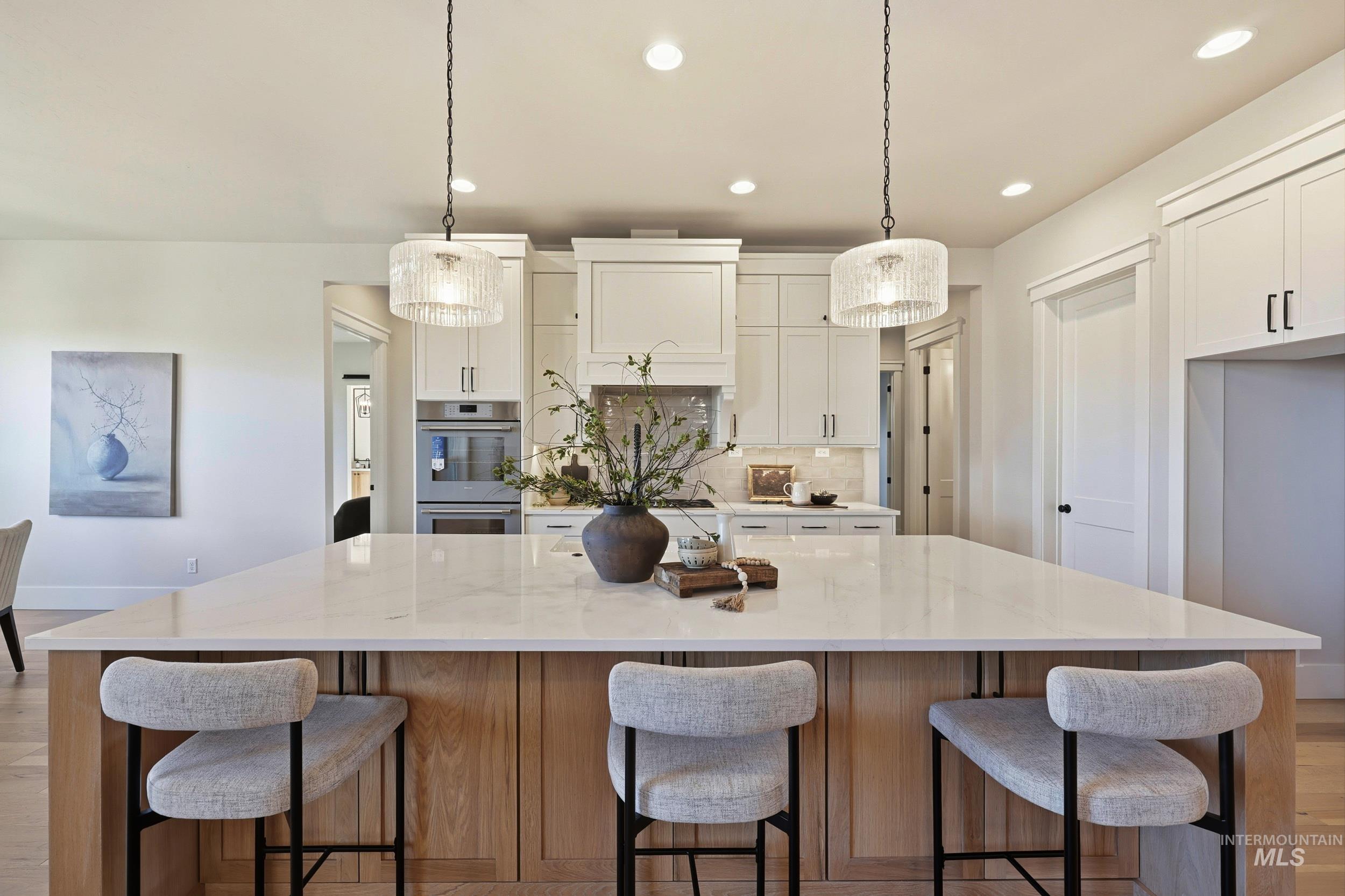 Kitchen with decorative backsplash, light wood-style flooring, decorative light fixtures, a breakfast bar area, and white cabinetry