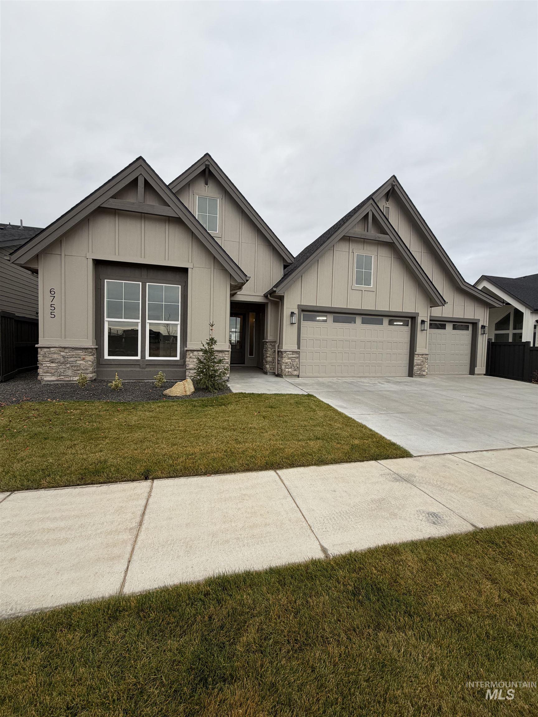 Craftsman-style home with board and batten siding, stone siding, a front yard, and concrete driveway