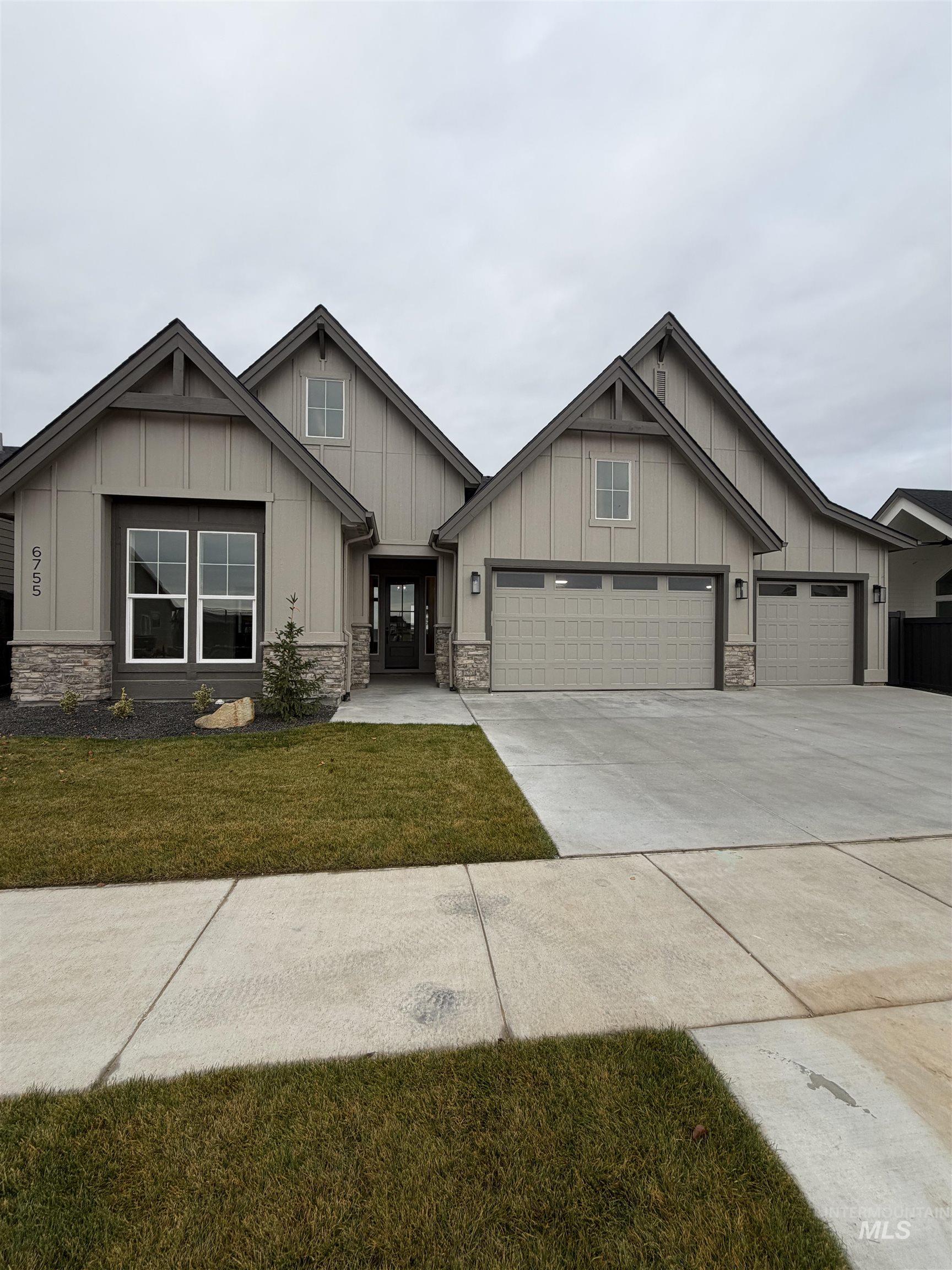 Craftsman-style house featuring board and batten siding, stone siding, driveway, and a front lawn