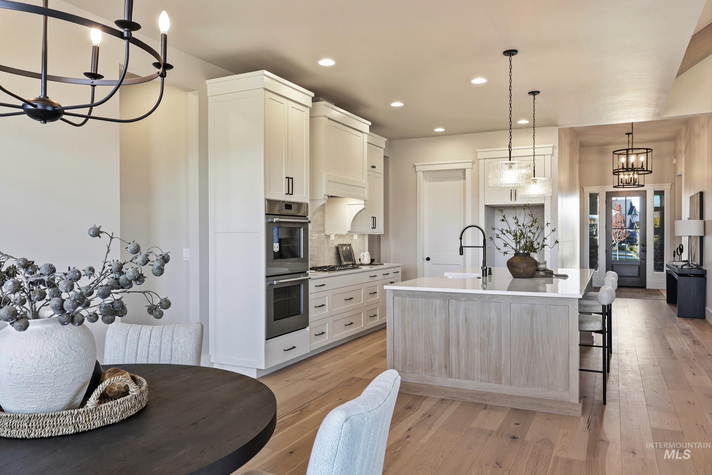 Kitchen featuring a chandelier, decorative light fixtures, white cabinets, light wood-style floors, and an island with sink