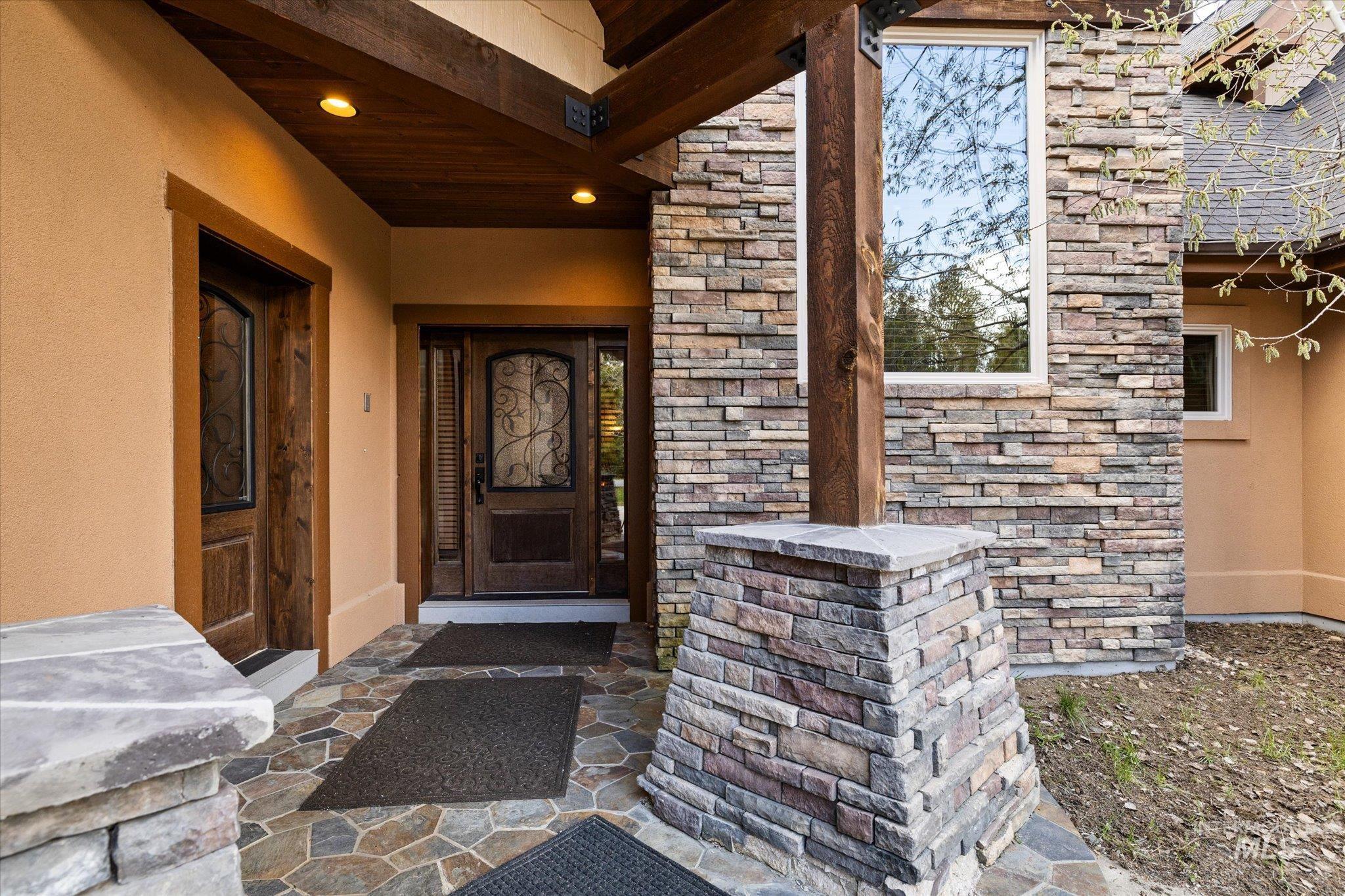 Stone facade and stucco exterior featuring a wood-finish entry door with decorative ironwork, a second wood-finish door, and a flagstone patio