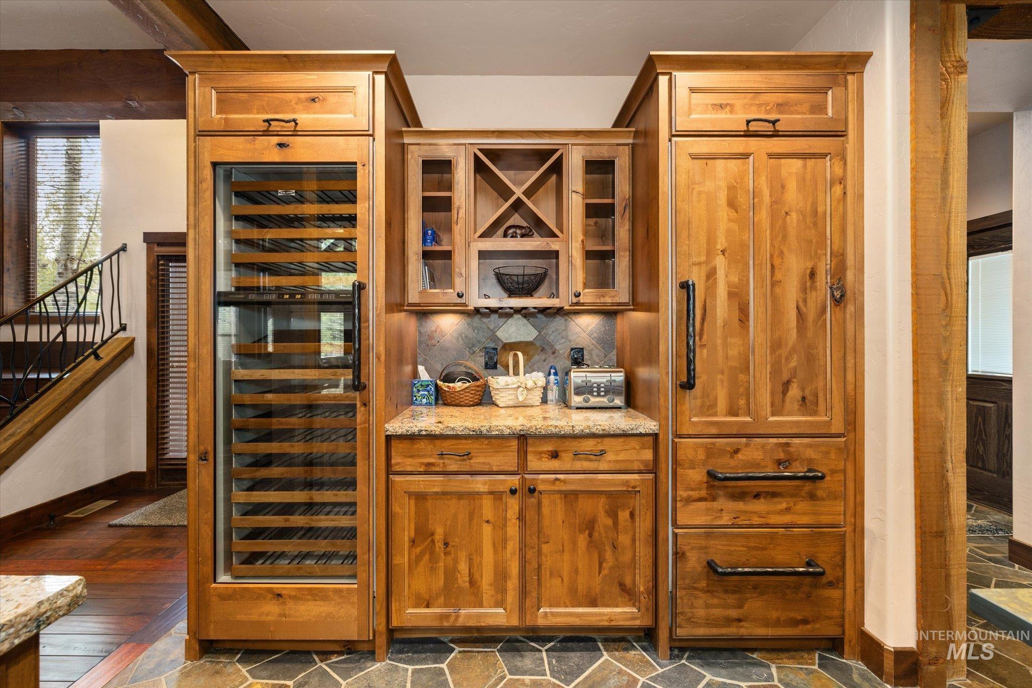 Built-in beverage center featuring a glass-front wine refrigerator, custom wood cabinetry, granite countertops, and stone tile backsplash