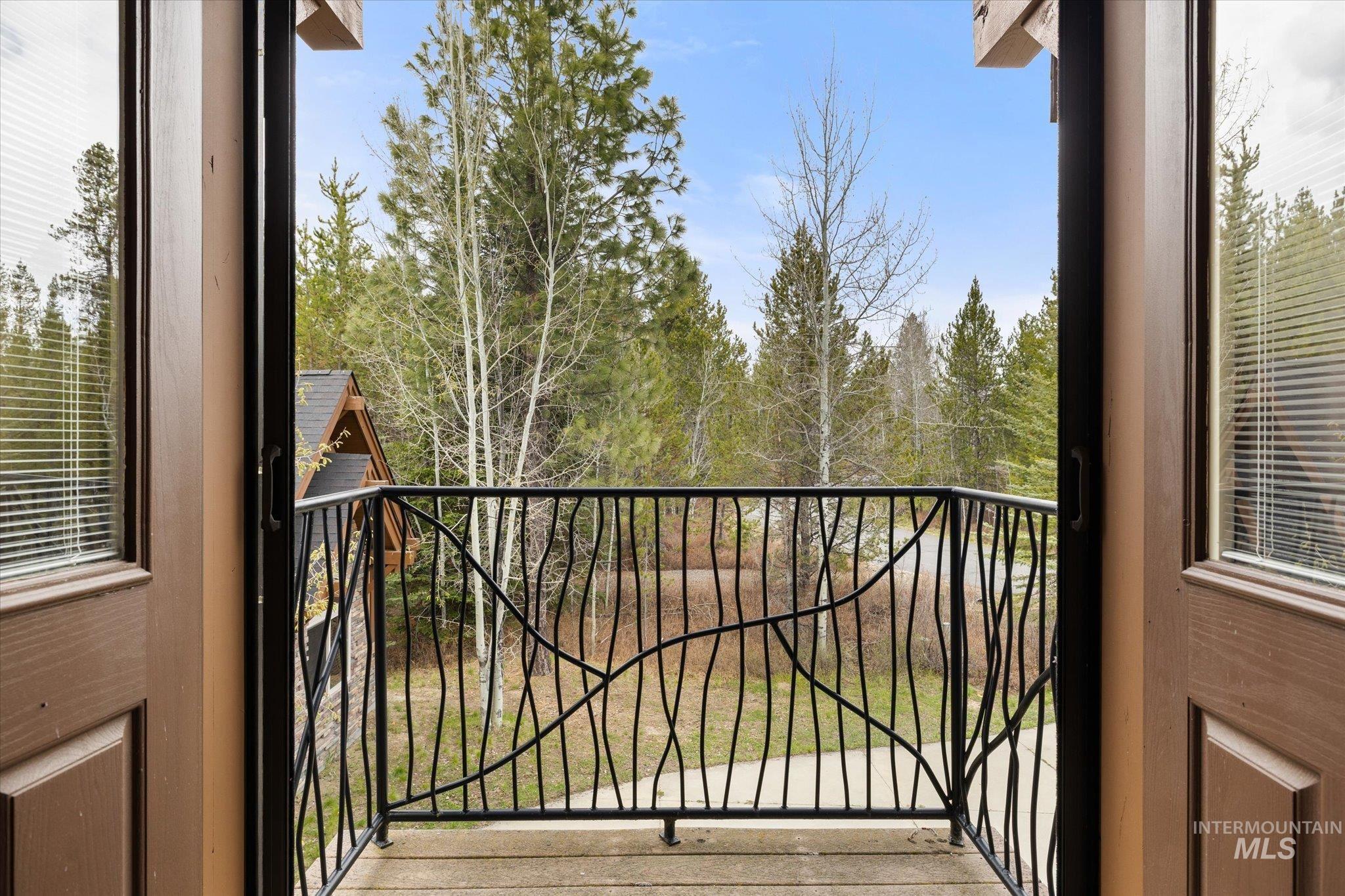 Private balcony with decorative wrought iron railing, wood-finish flooring, and natural wooded surroundings