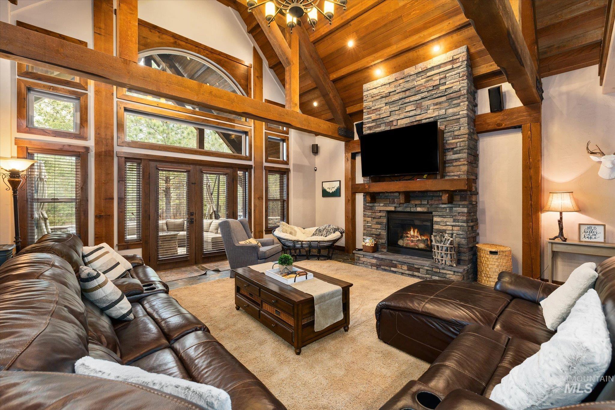 Great room featuring a floor-to-ceiling stone fireplace, exposed wood beams, vaulted wood-paneled ceiling, large windows, and glass patio doors