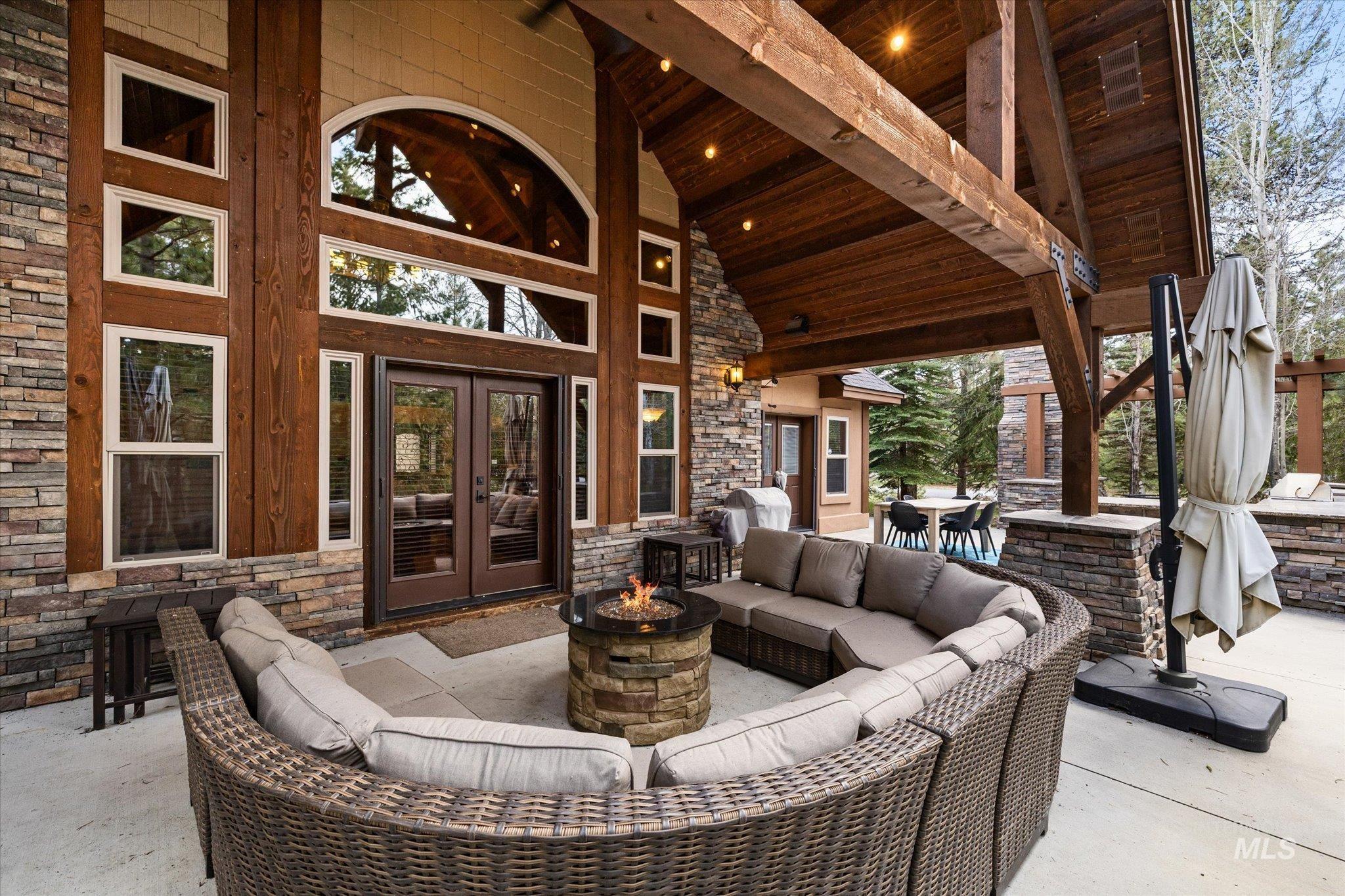Expansive outdoor living area featuring a stone-clad exterior, exposed timber beams, and a built-in fire pit