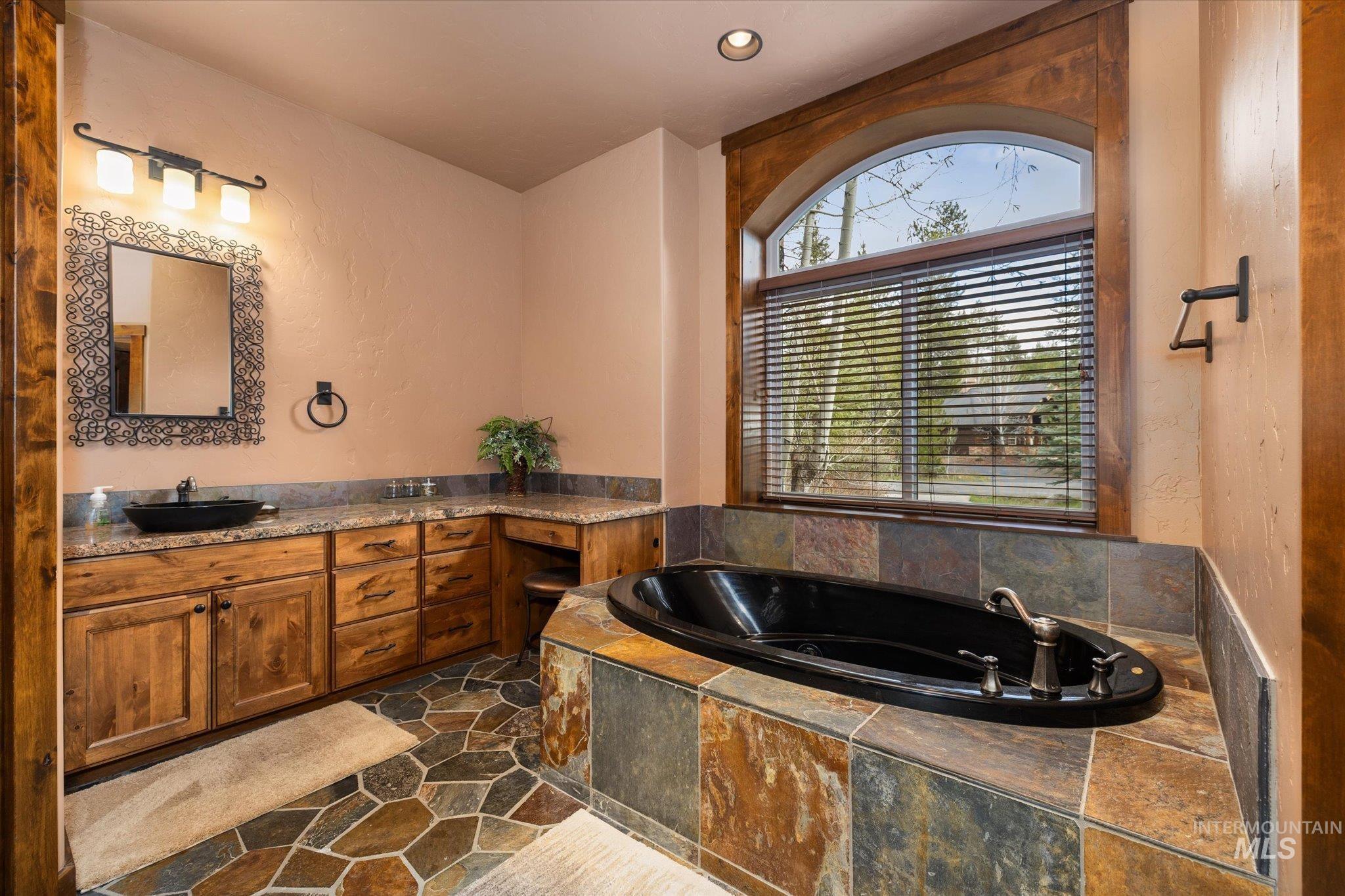 Spacious bathroom featuring a built-in soaking tub, a large arched window with blinds, and a dual vanity with vessel sinks