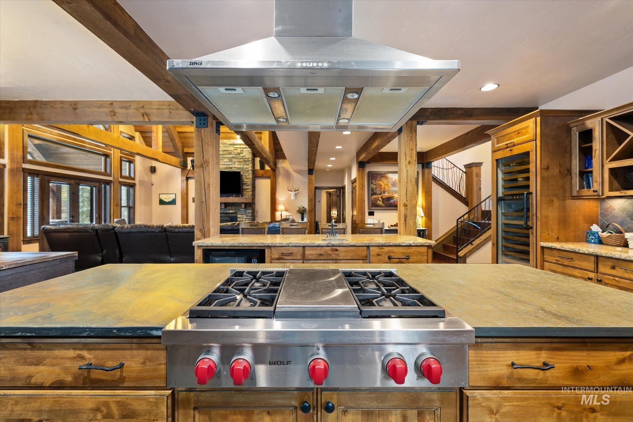 Gourmet kitchen island featuring a stainless steel gas range with a matching professional-grade vent hood, wood-finish cabinetry, and stone countertops