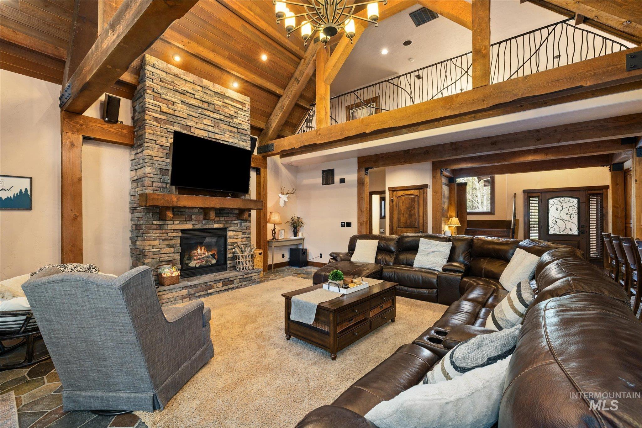 Spacious living area featuring a stone fireplace with a wood mantle, vaulted wood-beamed ceilings, a decorative wrought iron balcony, and a multi-level layout