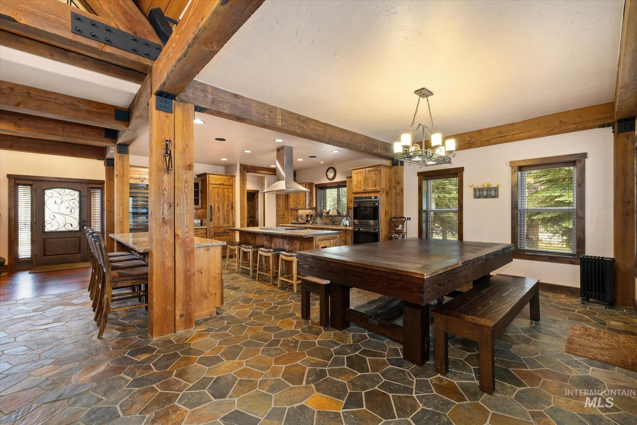 Spacious interior featuring exposed wooden beams, flagstone flooring, a large kitchen island with seating, a built-in oven, and a double-door entryway with decorative glass