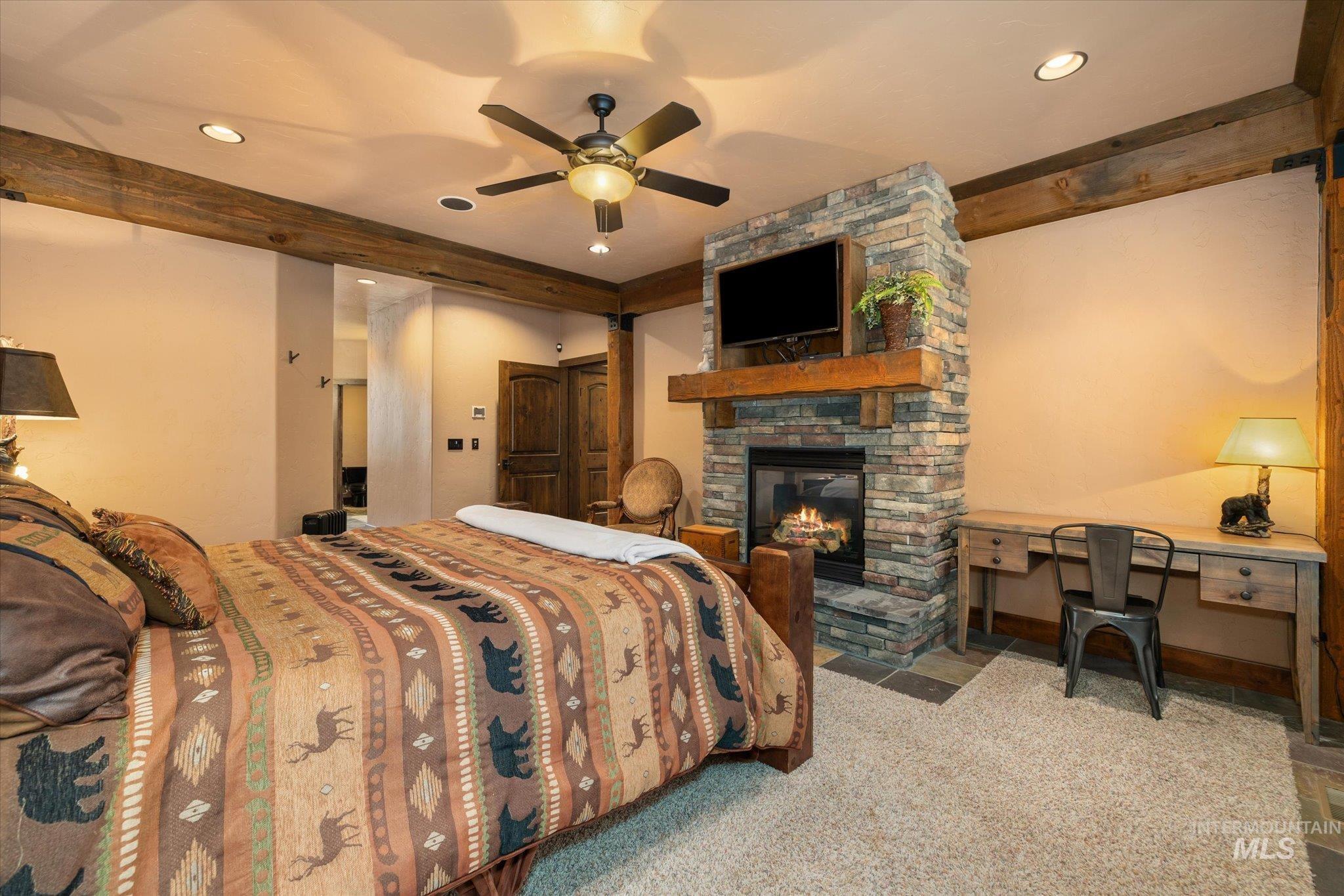 Bedroom featuring a stone fireplace with a wood mantle, a built-in television mount, and exposed wood ceiling beams