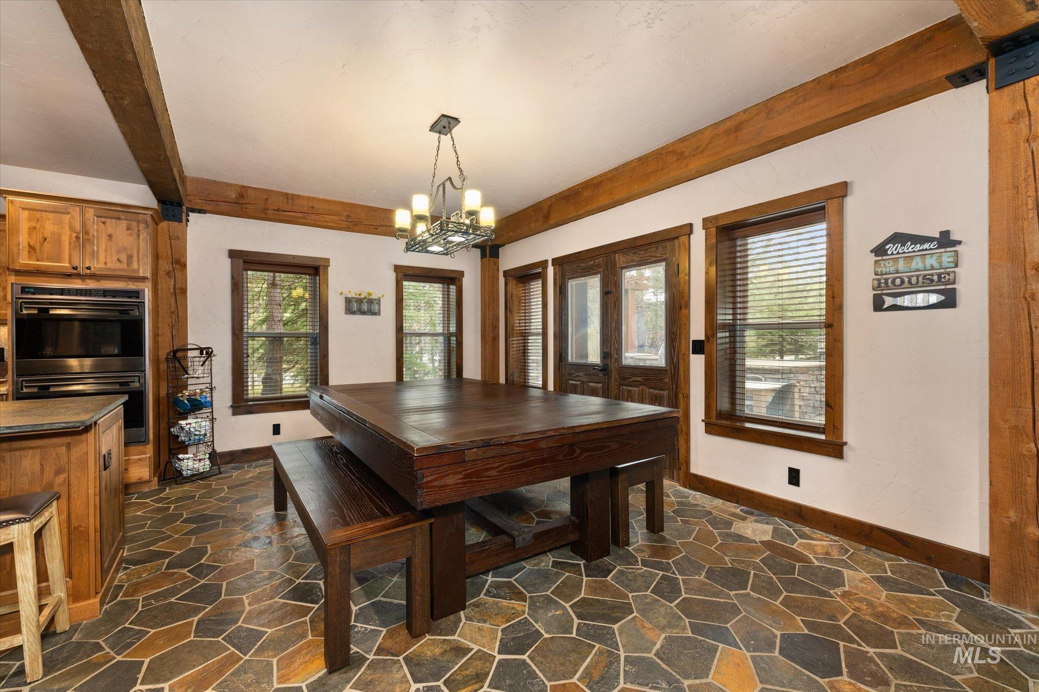 Spacious kitchen and dining area featuring natural wood beams, stone tile flooring, and double ovens