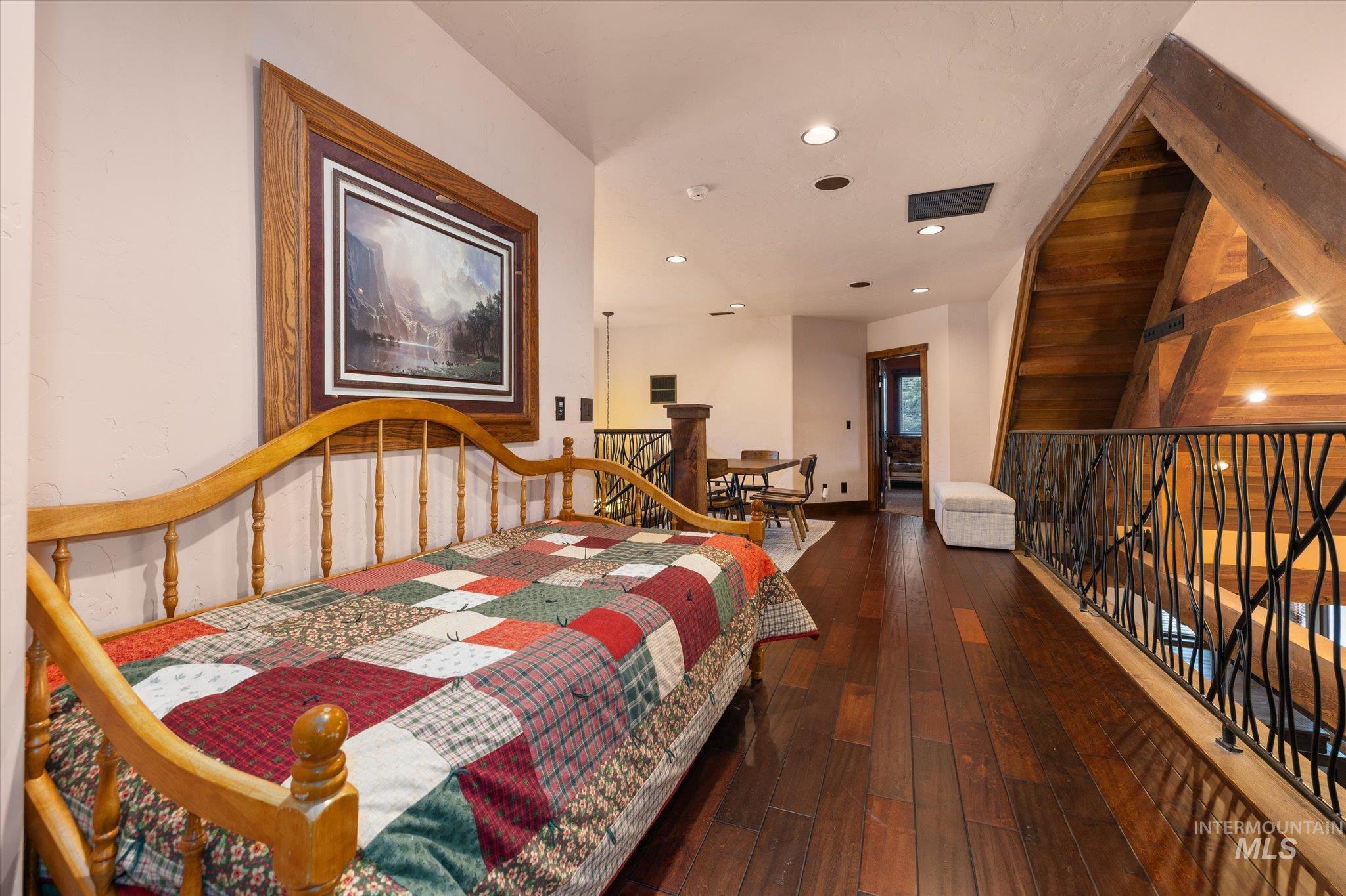 Loft space featuring rich wood-finish flooring and a wrought iron railing with organic-inspired detailing
