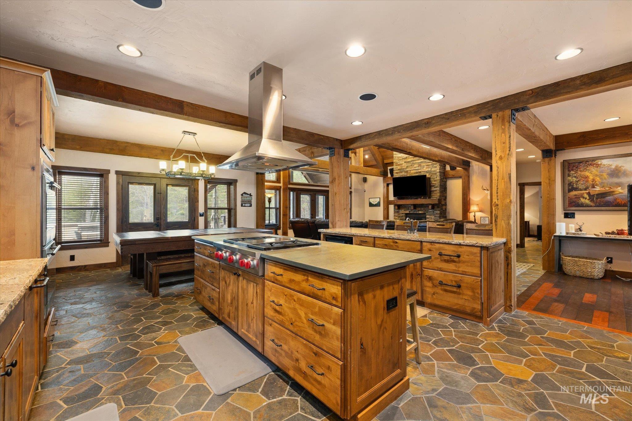 Kitchen featuring a large island with a built-in range, stainless steel hood vent, and abundant wood cabinetry