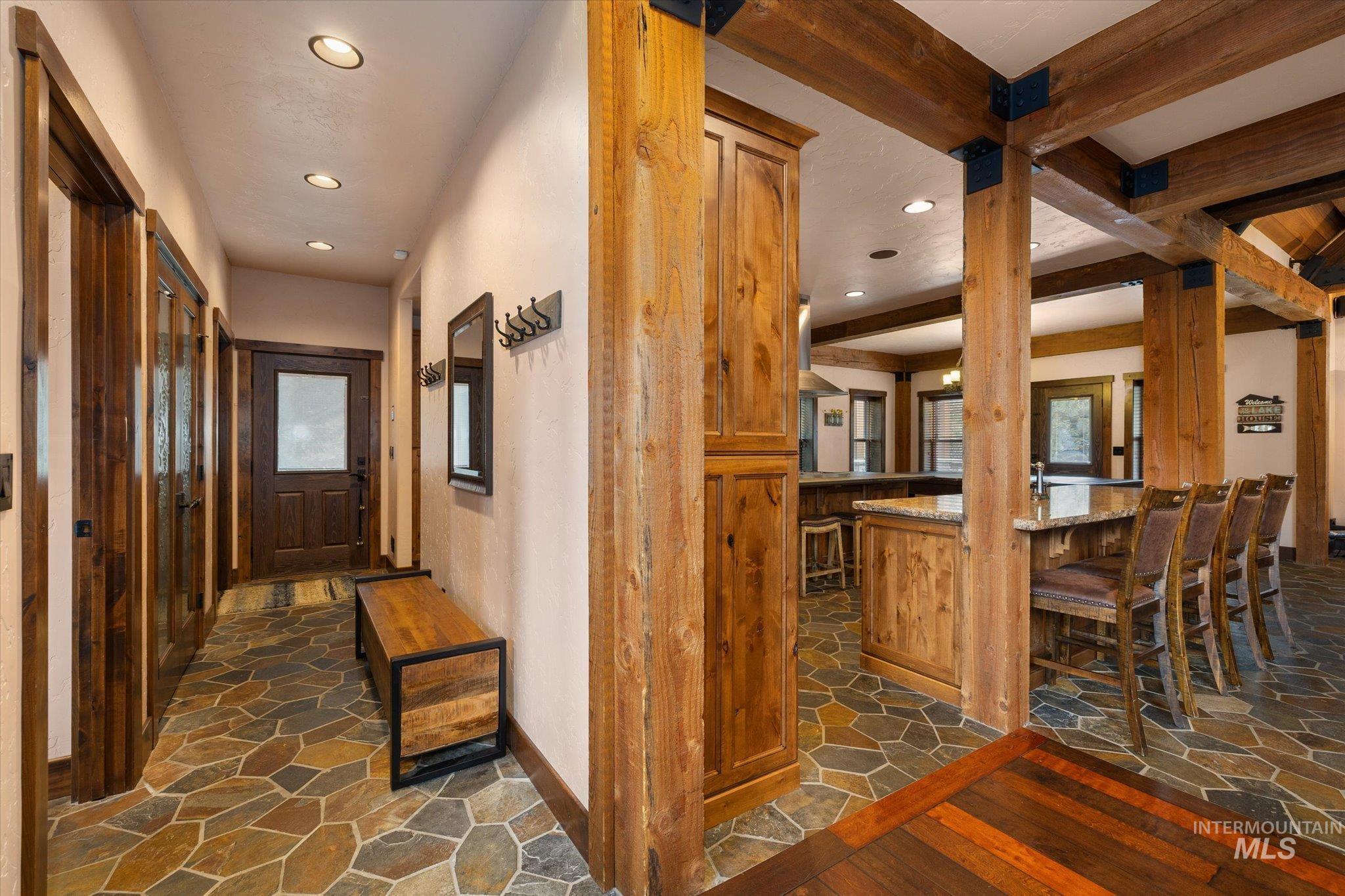 Foyer and kitchen area featuring natural wood beams, stone-finish flooring, recessed lighting, and rich wood cabinetry